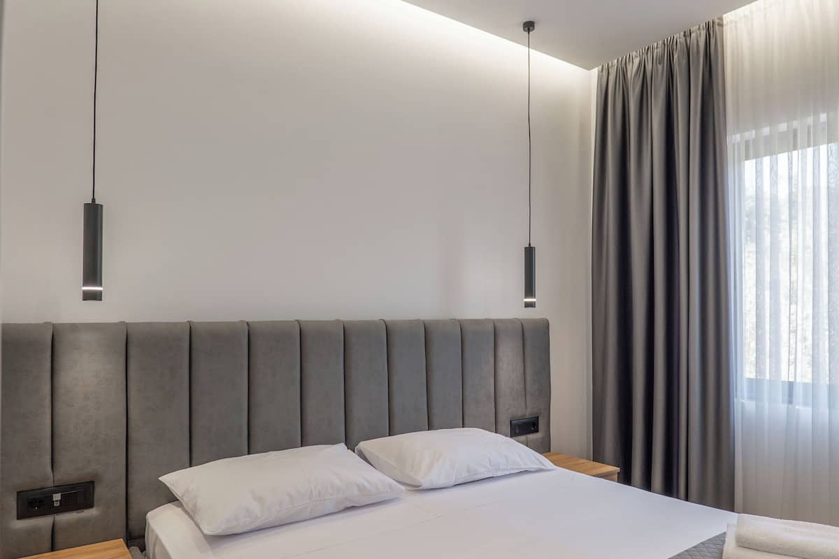 A modern hotel room with a large bed, bedside tables, and pendant lighting.