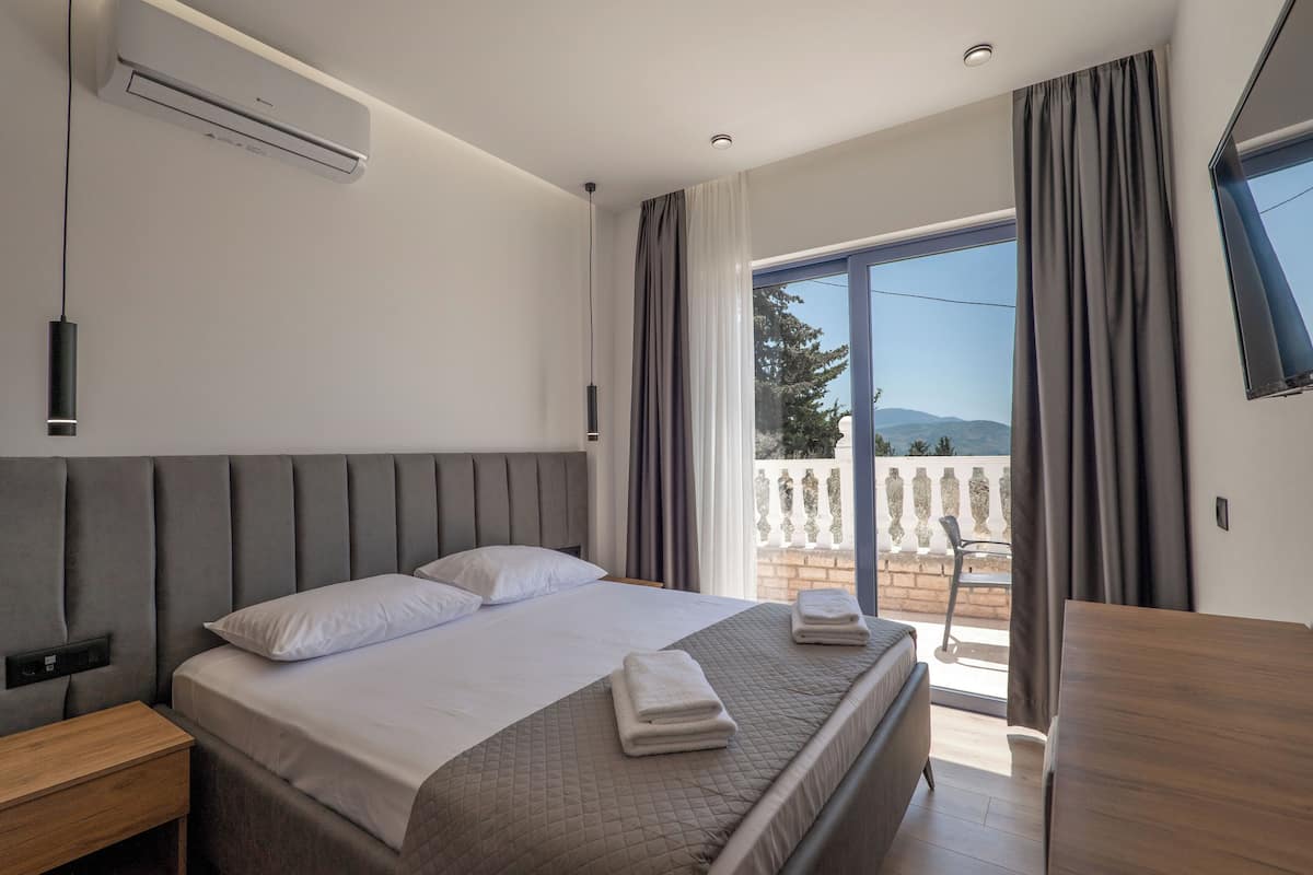 A modern hotel room with a large bed, a bedside table, a flat-screen TV, and a balcony with a view.