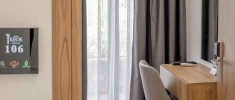 Habitación de hotel con un escritorio de madera, una silla, un televisor y una ventana con cortinas.