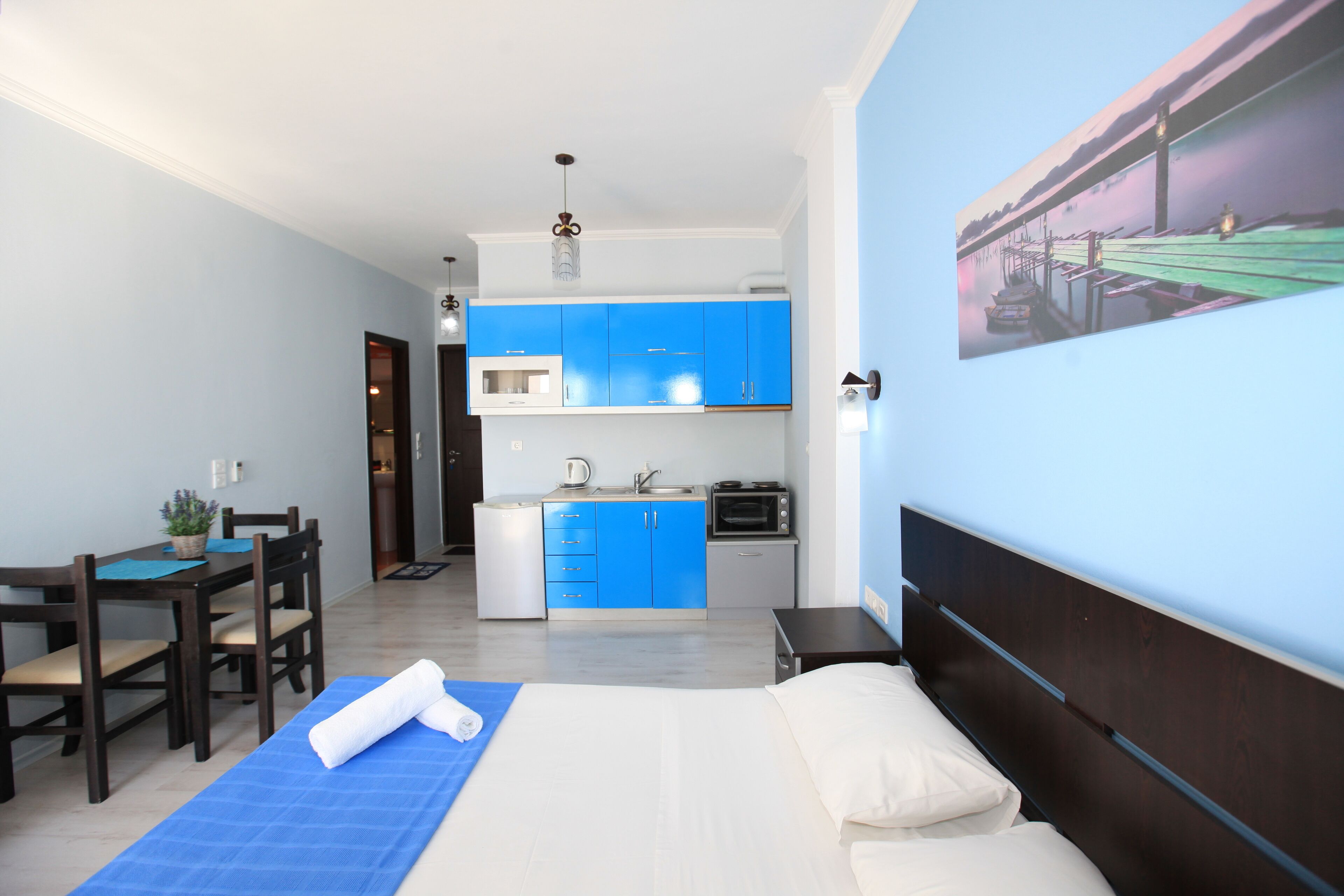 Una habitación de hotel compacta con cama, un pequeño kitchenette, un comedor y un cuadro en la pared.