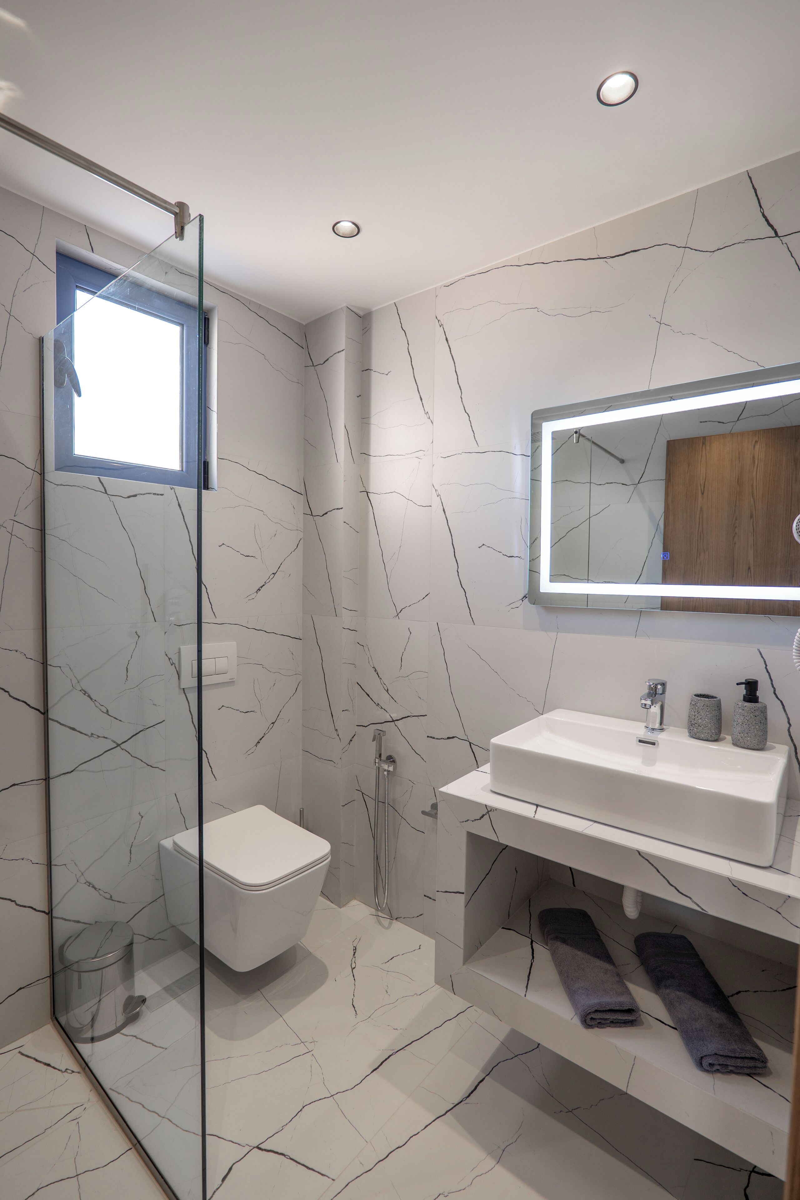 Ein modernes Badezimmer mit Duschkabine aus Glas, einer weißen Toilette, einem Waschbecken mit Spiegel und einem Handtuchhalter.