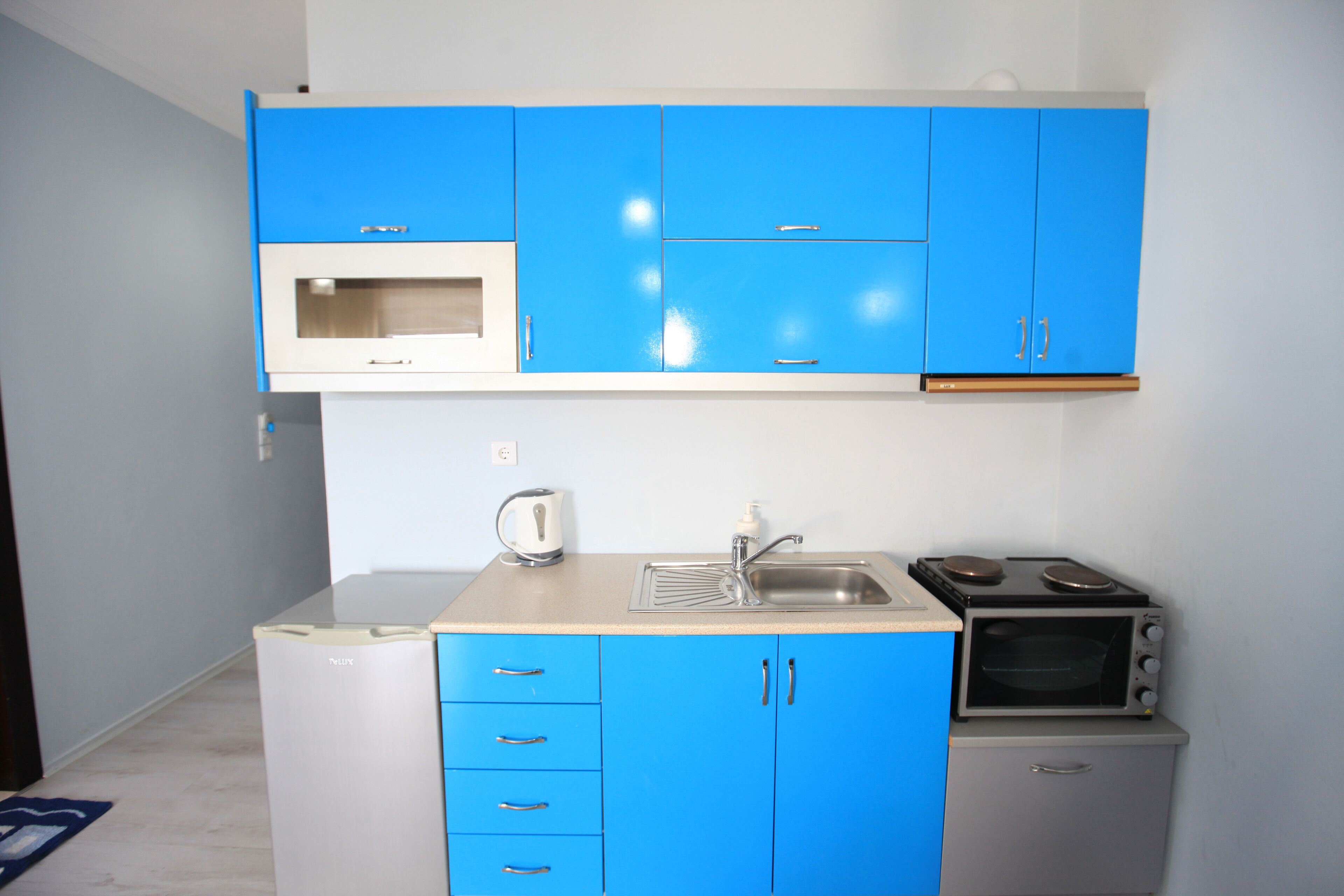 Una cocina compacta con armarios azules, un microondas, un hervidor, un lavamanos y una estufa.