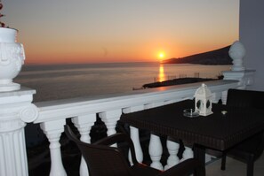A balcony with a view of the sunset over the sea, a white balustrade, and a table with chairs. - Hotel Keos (Sarandë)