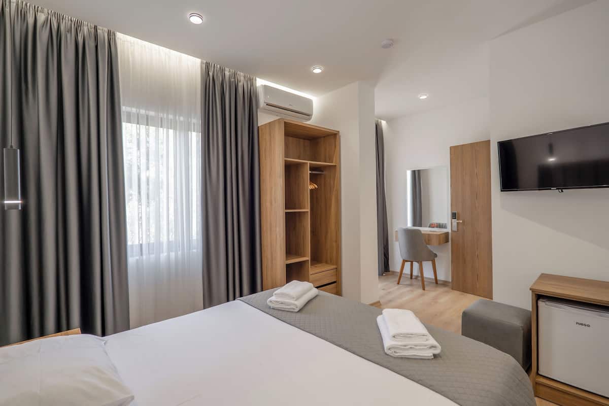 A modern hotel room with a large bed, a wardrobe, a desk, and a television.