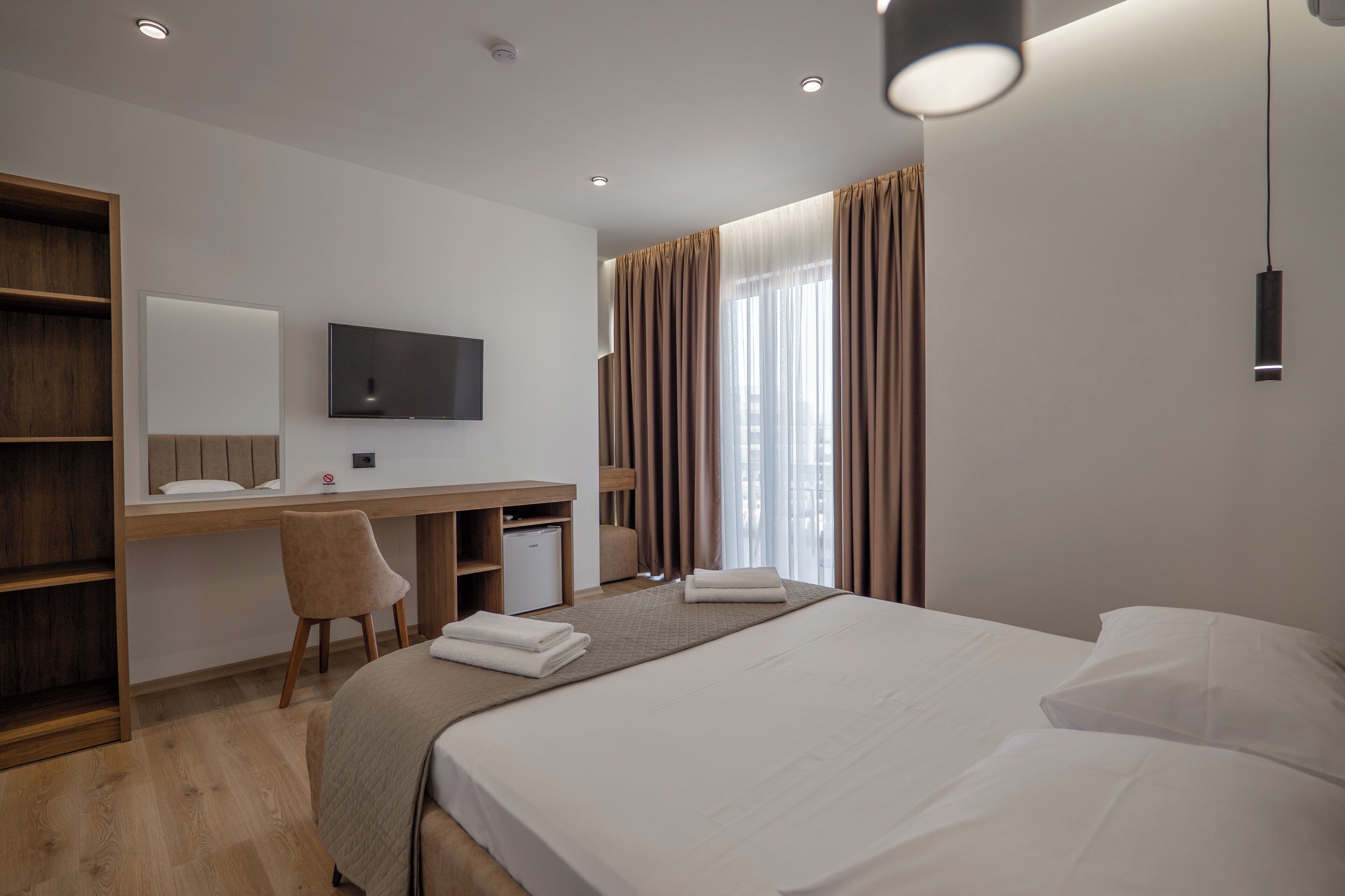 A modern hotel room with a large bed, a desk with a chair, a television, and a wardrobe.