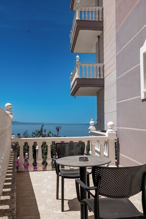 A balcony with a table and chairs, overlooking a body of water. - Hotel Keos (Sarandë)