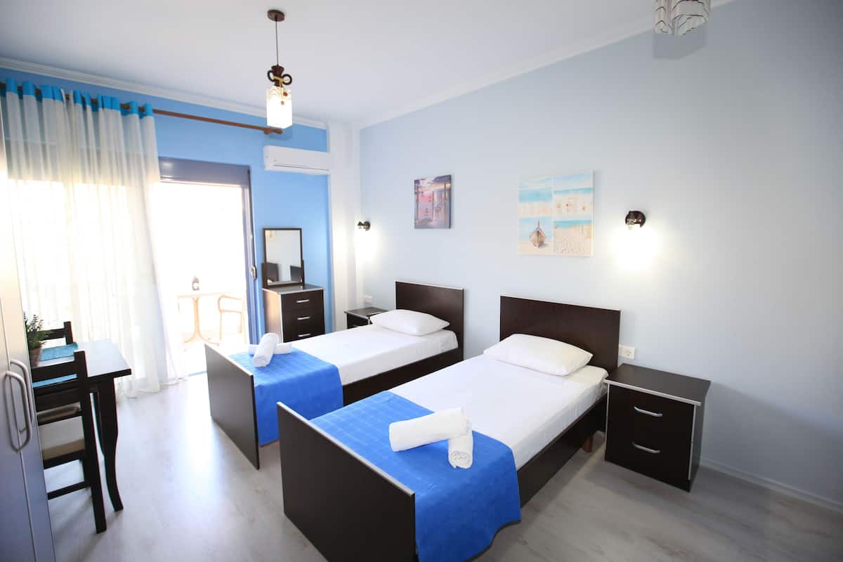 A hotel room with two beds, a desk, and a chair. There are two bedside tables and a wall-mounted lamp.