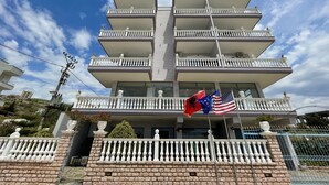 A multi-story building with balconies, a brick base, and a flag. - Hotel Keos (Sarandë)