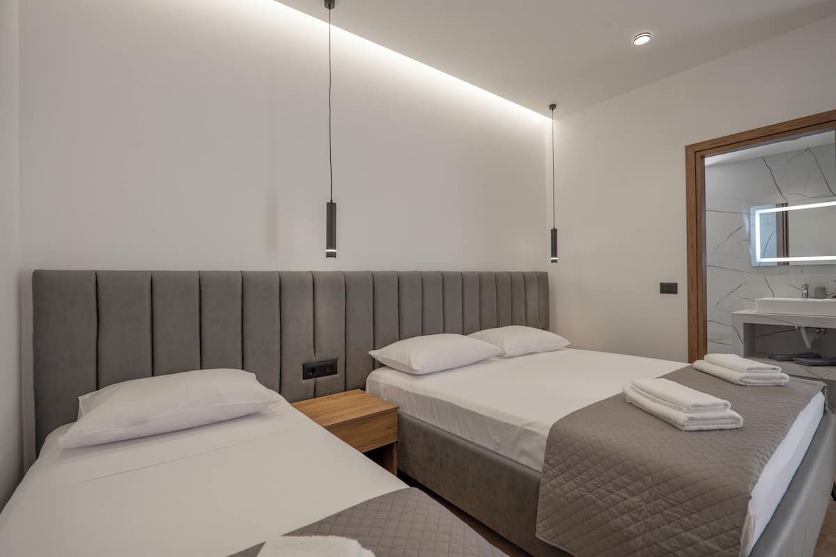 A hotel room with two beds, a wooden nightstand, a modern pendant light, a mirror, and a bathroom with a marble countertop.