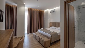 A modern hotel room with a wooden bed, a bench, a desk, and a shower area. - Hotel Keos (Sarandë)
