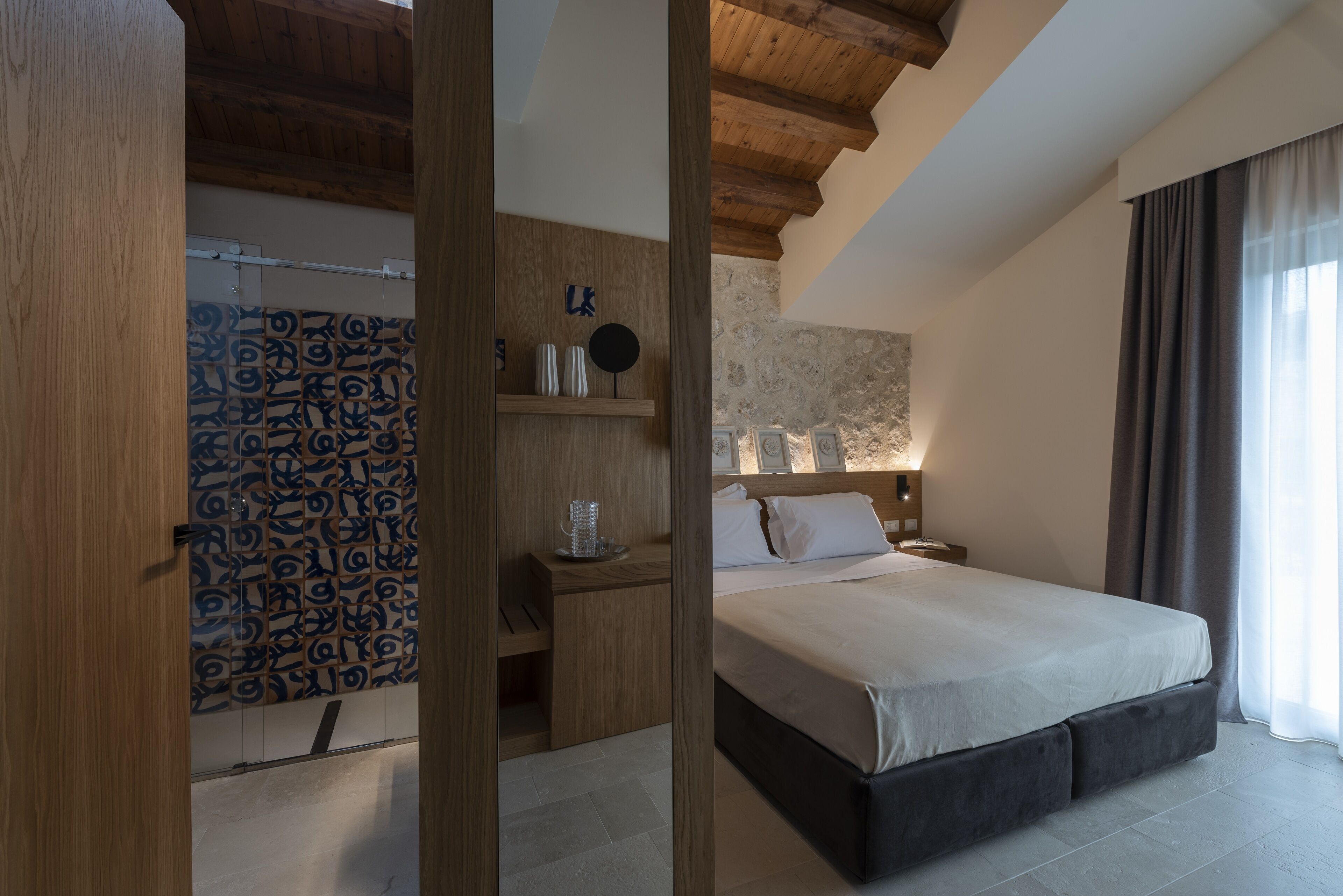 A bedroom with a bed, wooden headboard, bedside table, and a patterned wall.