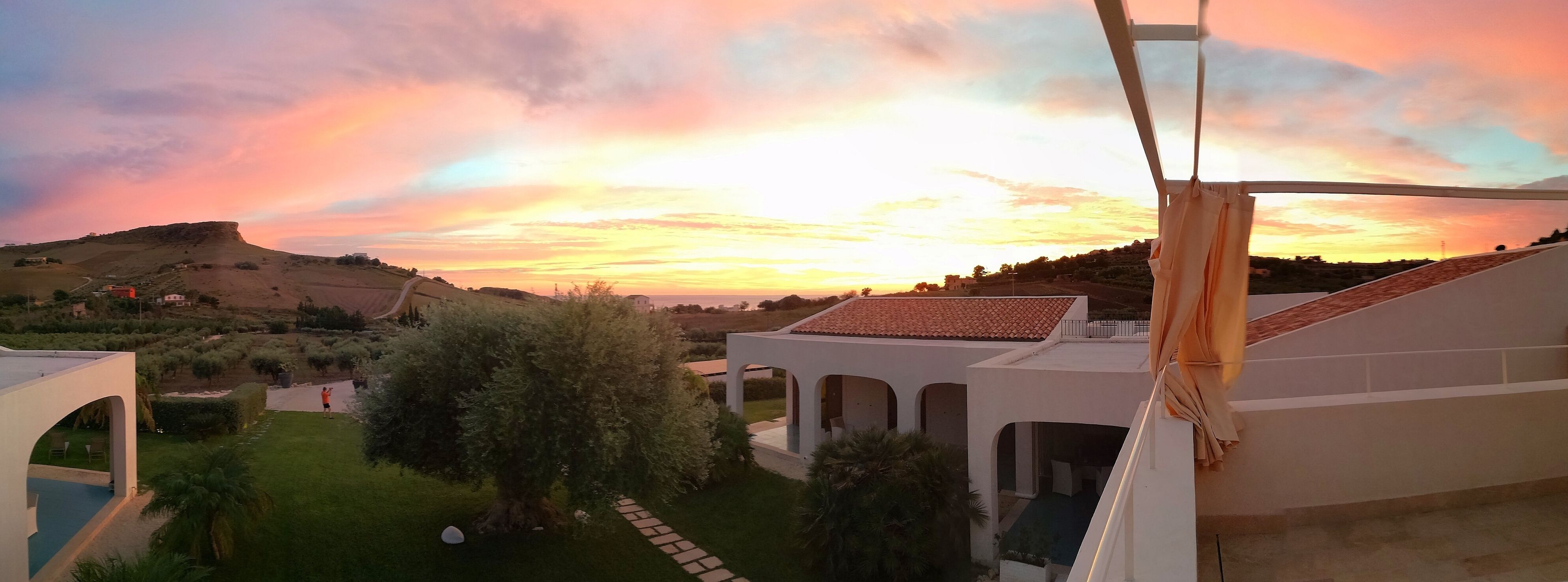A residential area with a view of a sunset over rolling hills, a pathway, and a white building with arches.