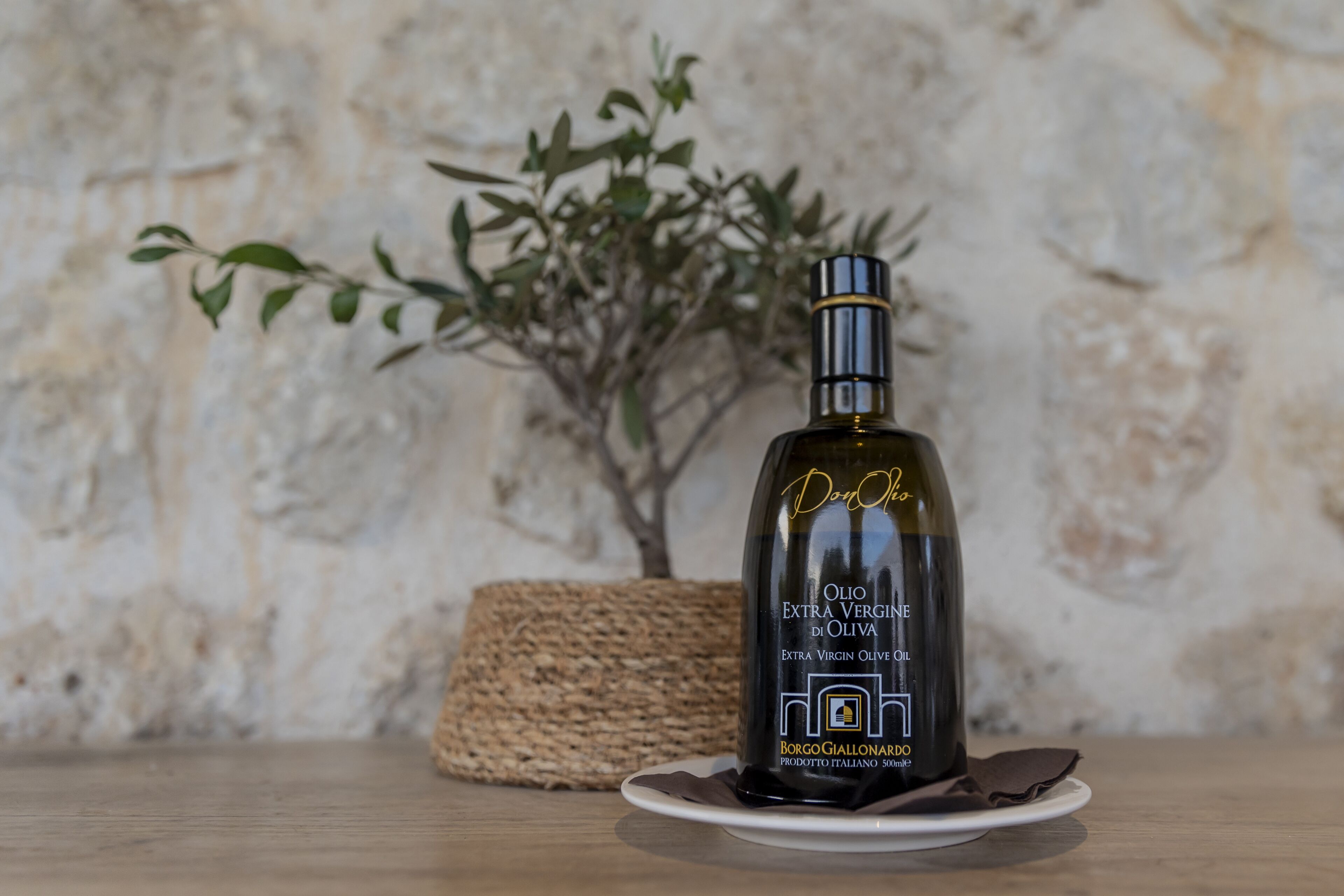 Une bouteille d’huile d’olive extra vierge sur une assiette blanche, avec un panier tressé et une plante en arrière-plan.
