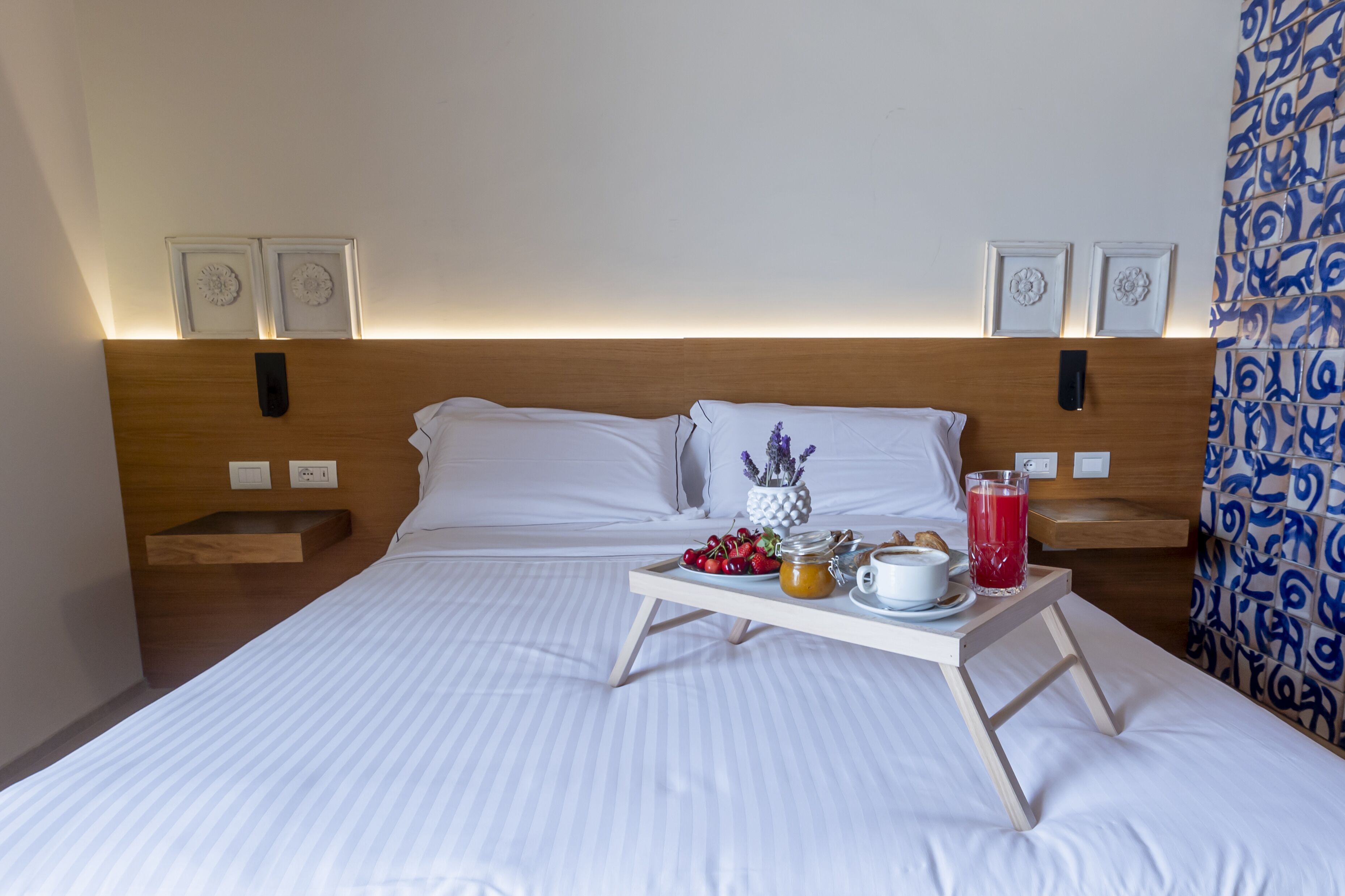 A neatly made bed with a tray of breakfast items, including fruits, a cup, and a glass of juice.