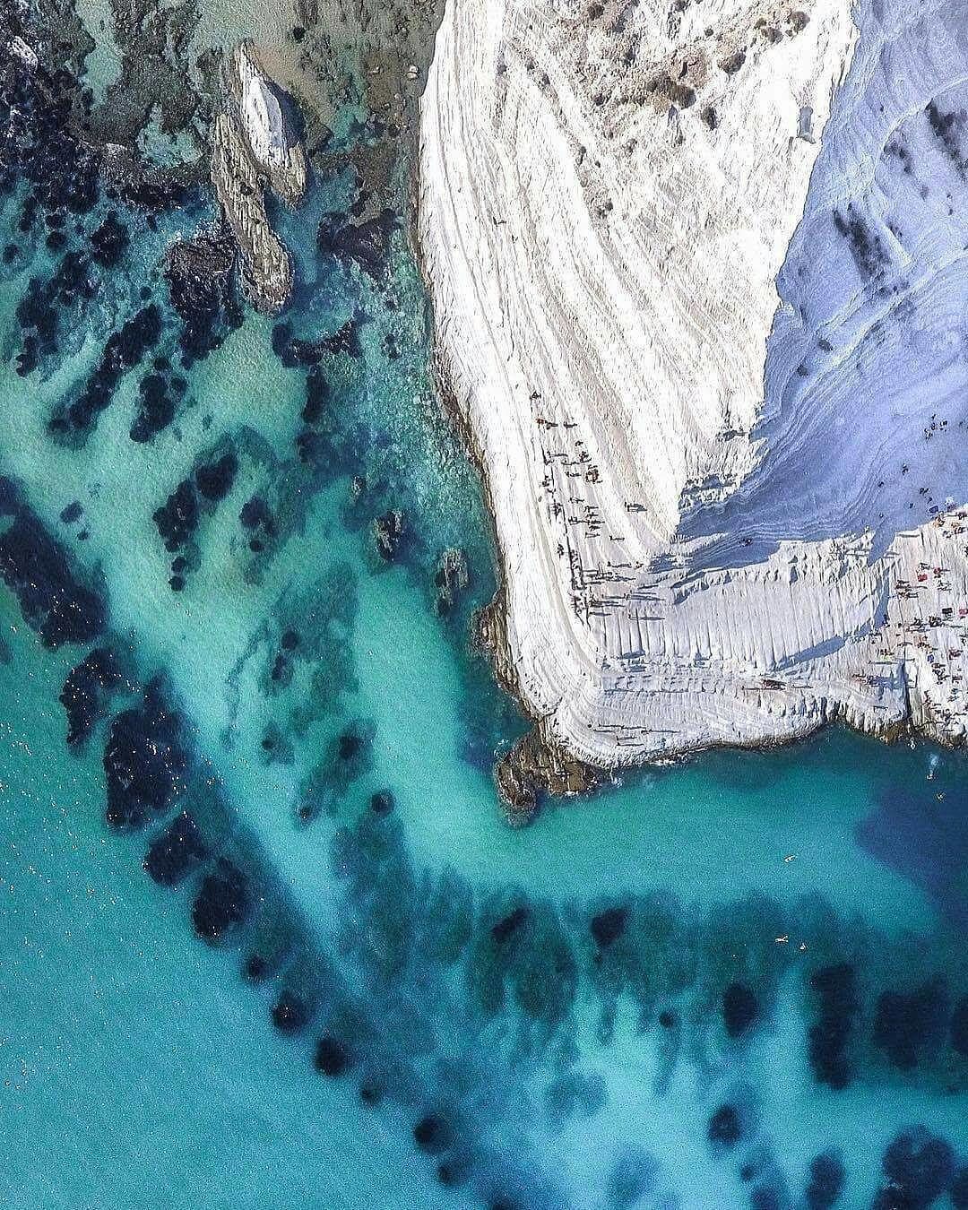 Eine Küstenklippe mit felsigem Ufer und klarem, türkisblauem Wasser.