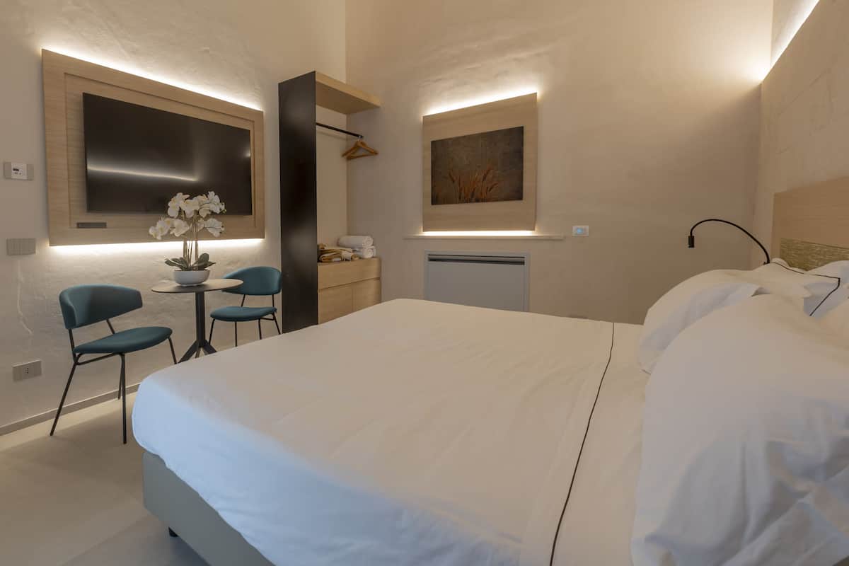 Une chambre d’hôtel moderne dotée d’un grand lit, d’un bureau avec des chaises, d’un téléviseur à écran plat et d’œuvres d’art accrochées aux murs.