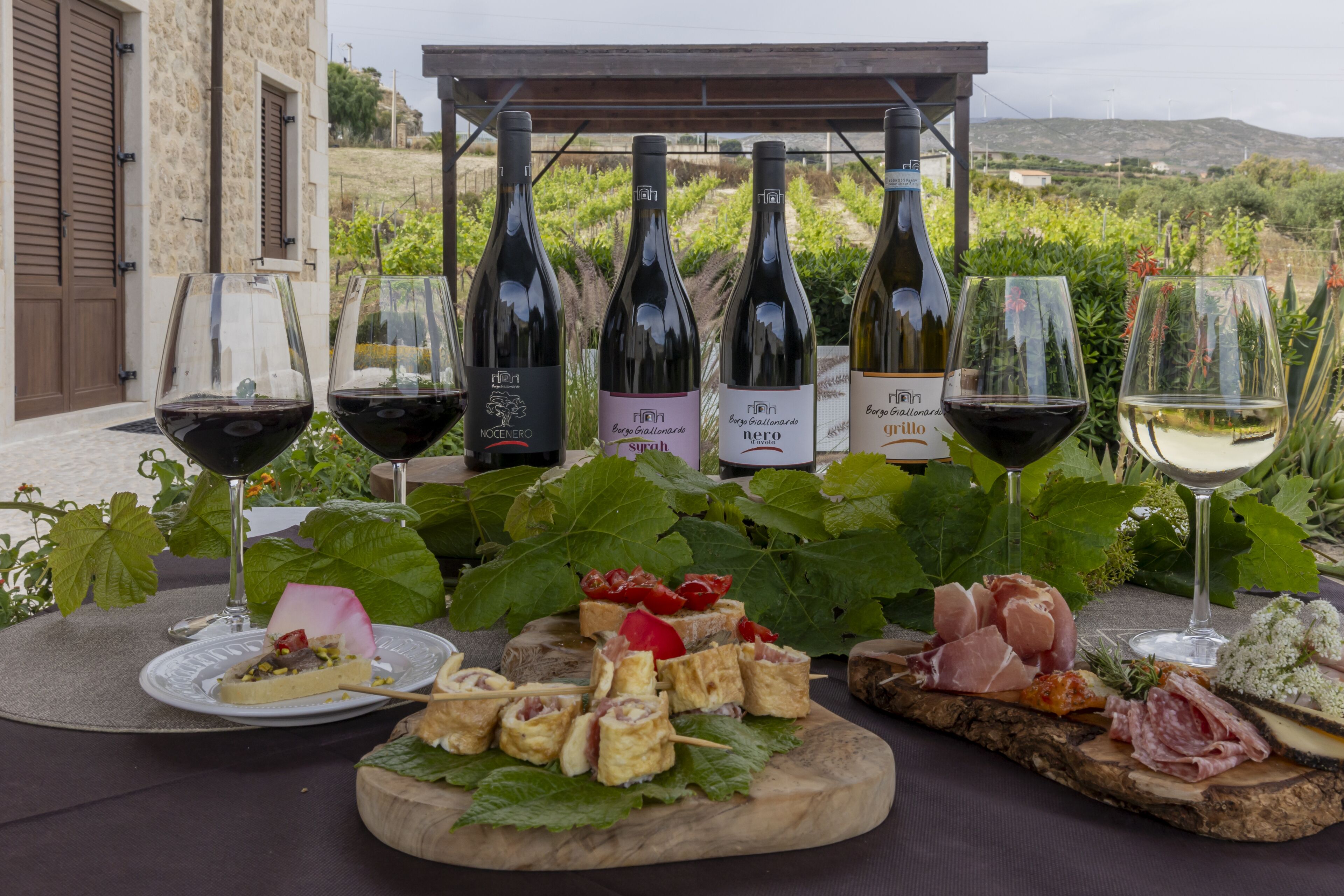 Une table dressée avec des bouteilles de vin, des verres et une variété de plats, notamment du fromage, de la charcuterie et des légumes.