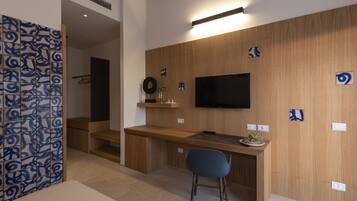 A modern hotel room with a wooden desk, a flat-screen TV mounted on the wall, a blue chair, and a decorative wall panel.