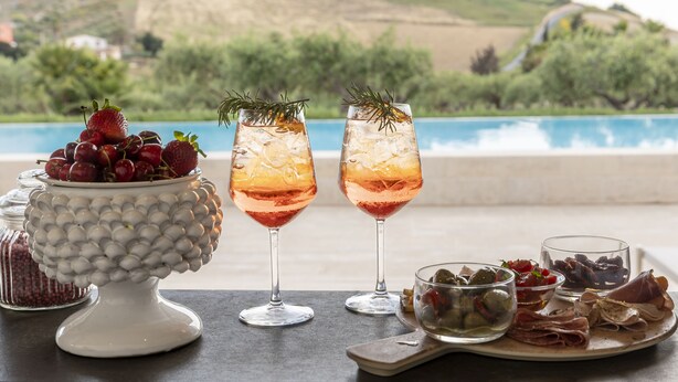 Una mesa con dos vasos de bebidas heladas, un cuenco de fresas y una bandeja de carnes y aceitunas.