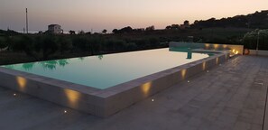 A rectangular infinity pool with a clear edge, surrounded by a stone deck and low lighting. - Borgo Giallonardo (Realmonte)