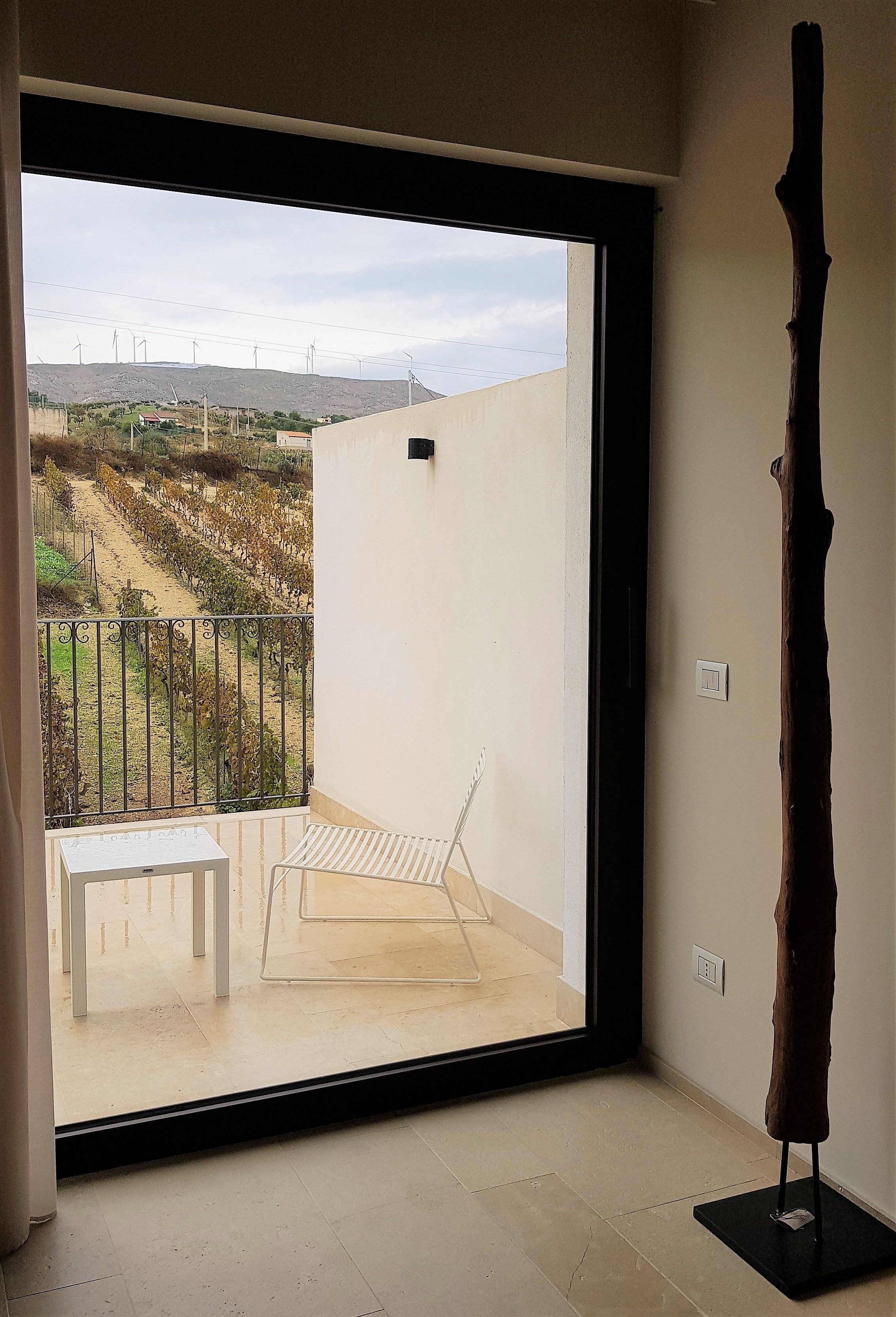 A room with a large sliding glass door leading to an outdoor balcony with a metal railing, a white table, and a wooden sculpture.