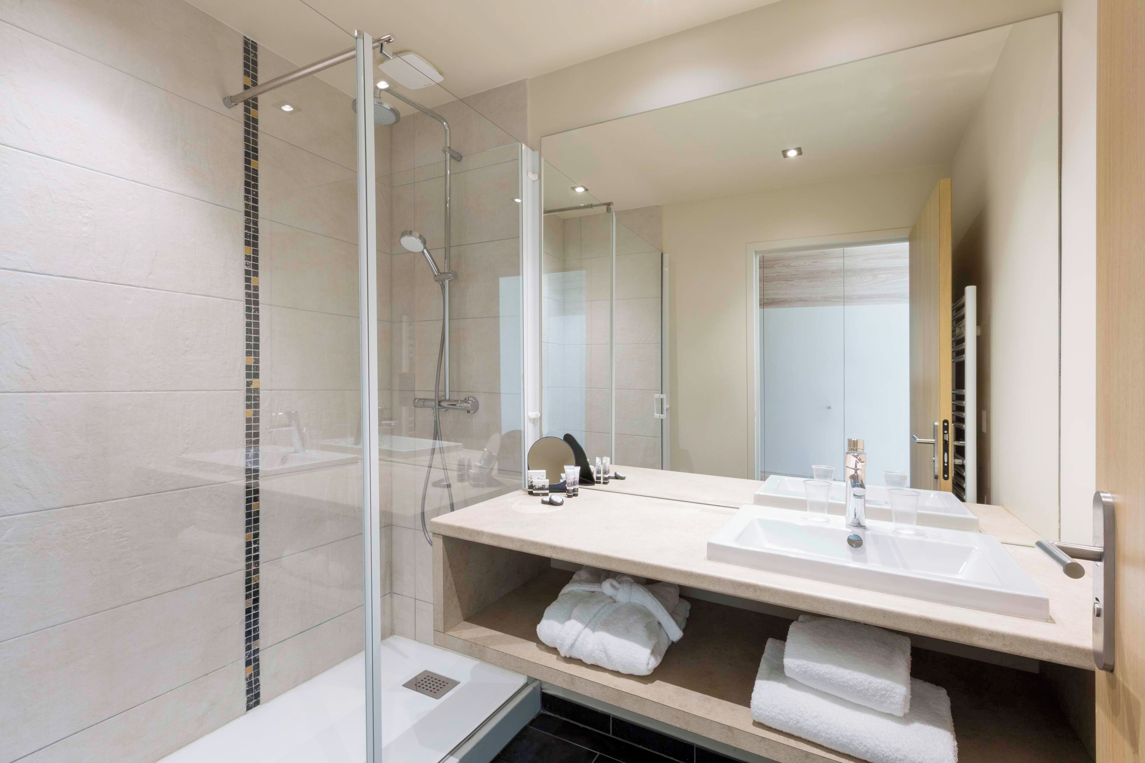 A modern bathroom with a glass-enclosed shower, a large mirror, and a vanity with two sinks.