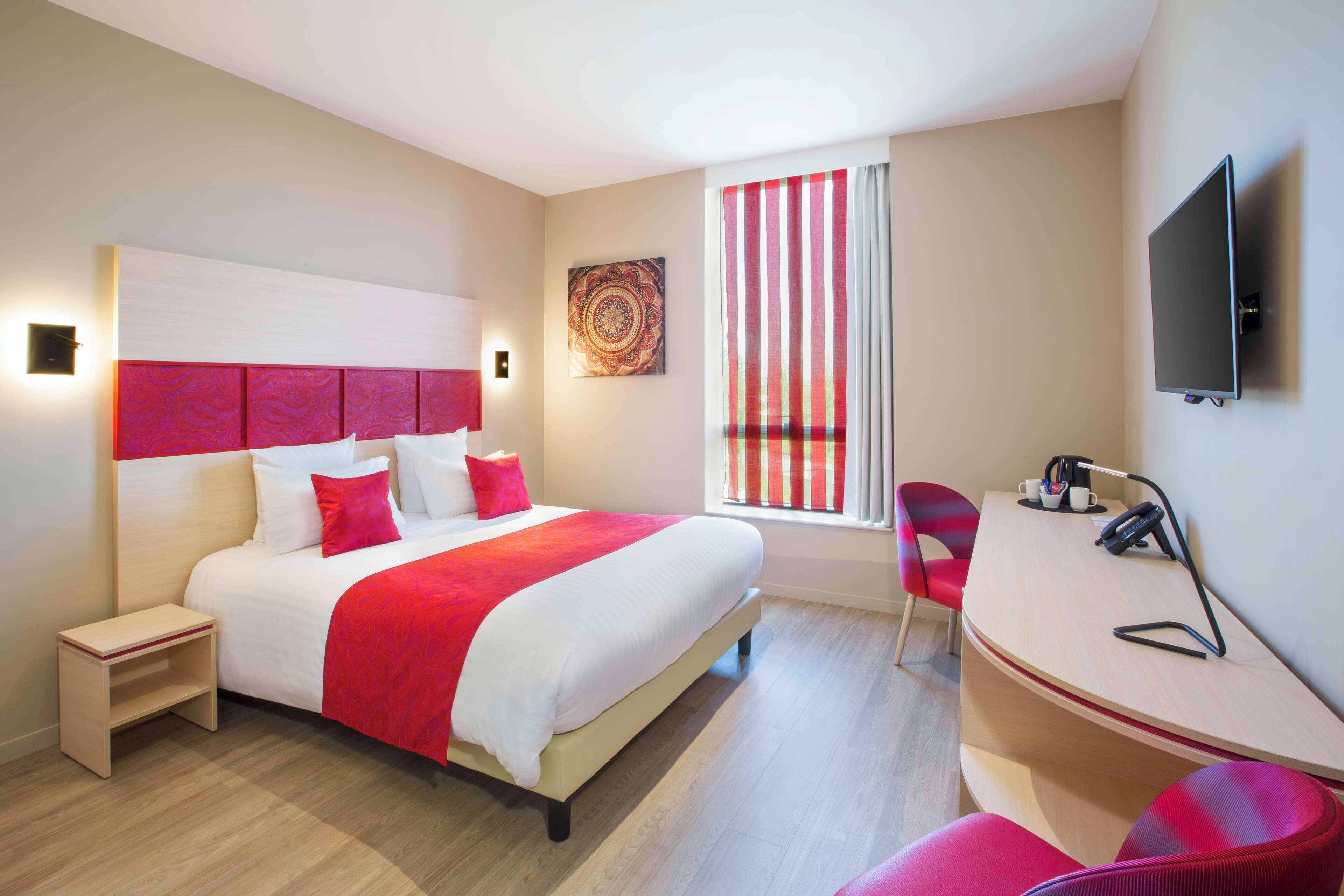 Habitación de hotel moderna con una cama grande, un escritorio con silla, televisión y ventana con cortinas.