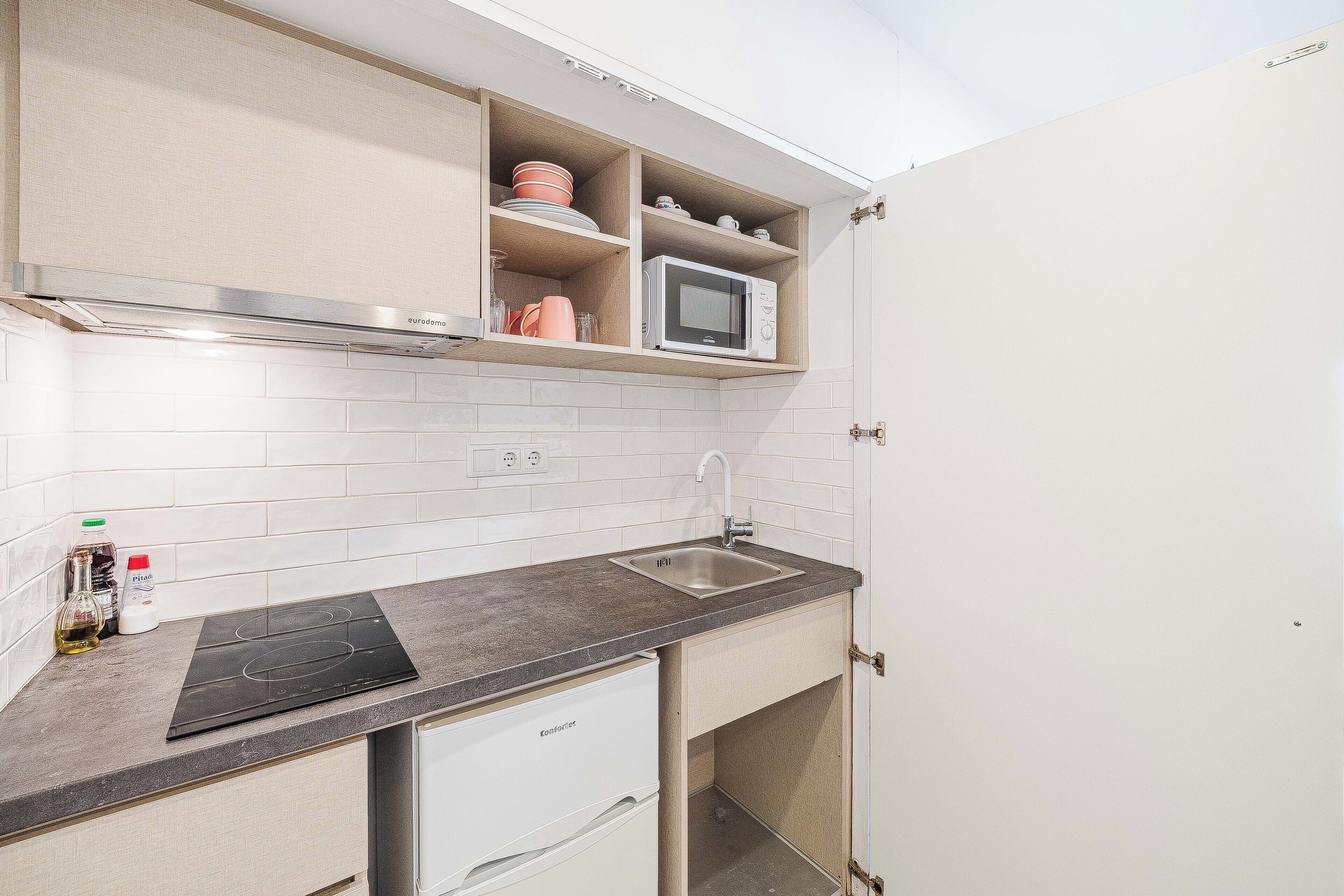 Una cocina compacta con microondas integrado, un lavamanos y un lavavajillas pequeño.