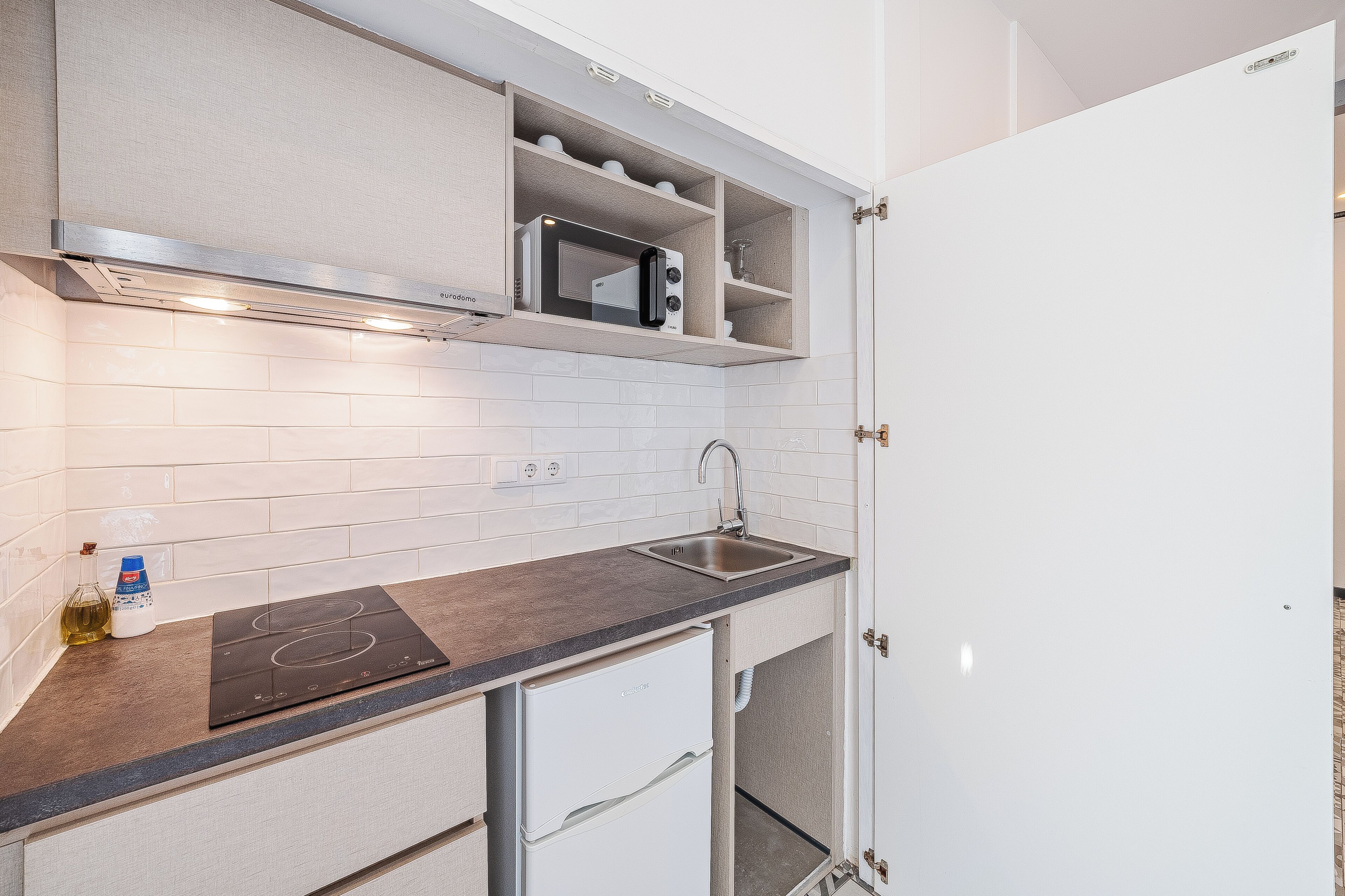 A compact kitchen with a built-in microwave, a stainless steel sink, and a compact refrigerator.