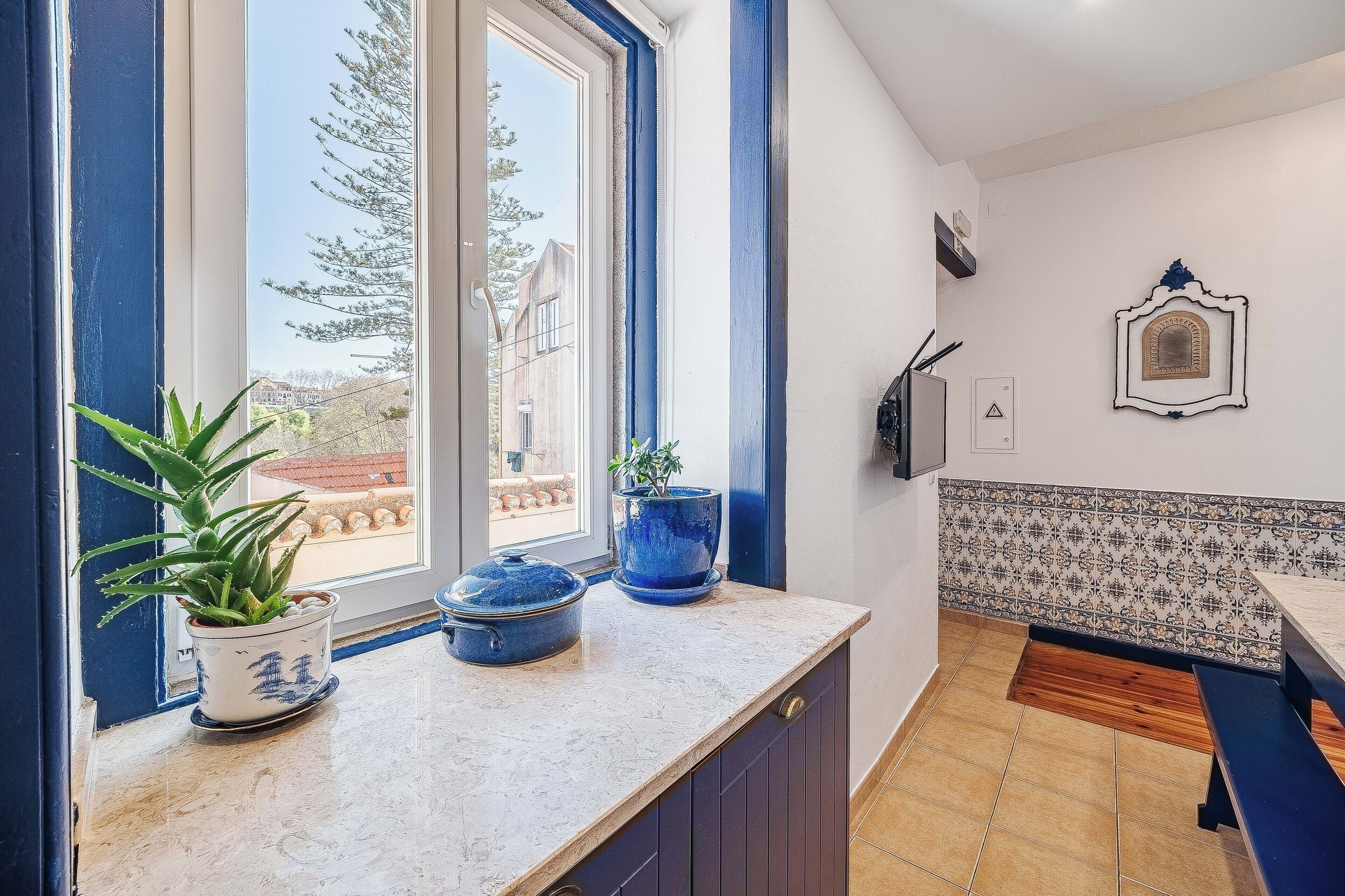 Une cuisine avec une fenêtre, des plantes en pot, un mur recouvert de carreaux et un banc.