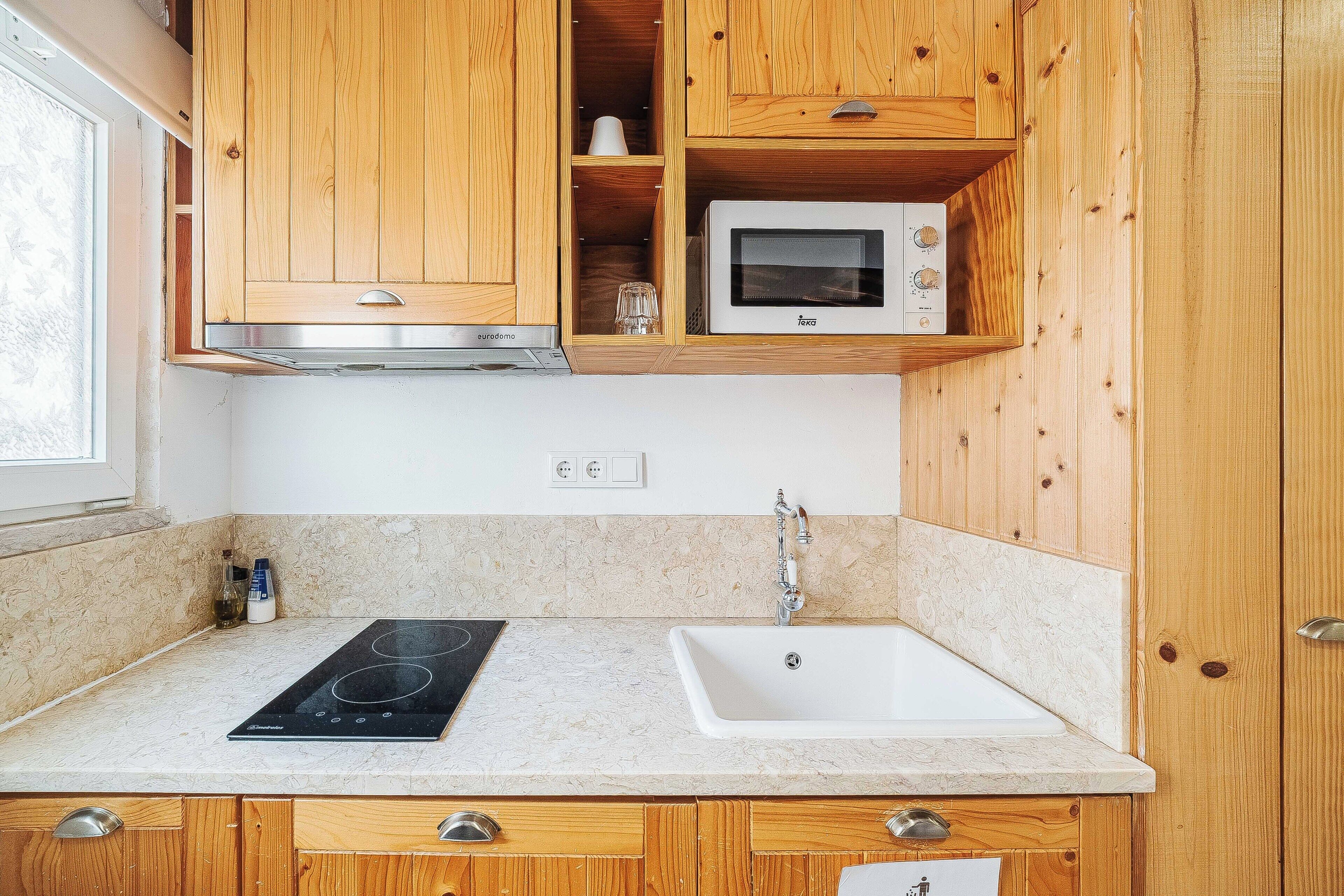 Una cocina con armarios de madera, microondas, placa de inducción y fregadero.