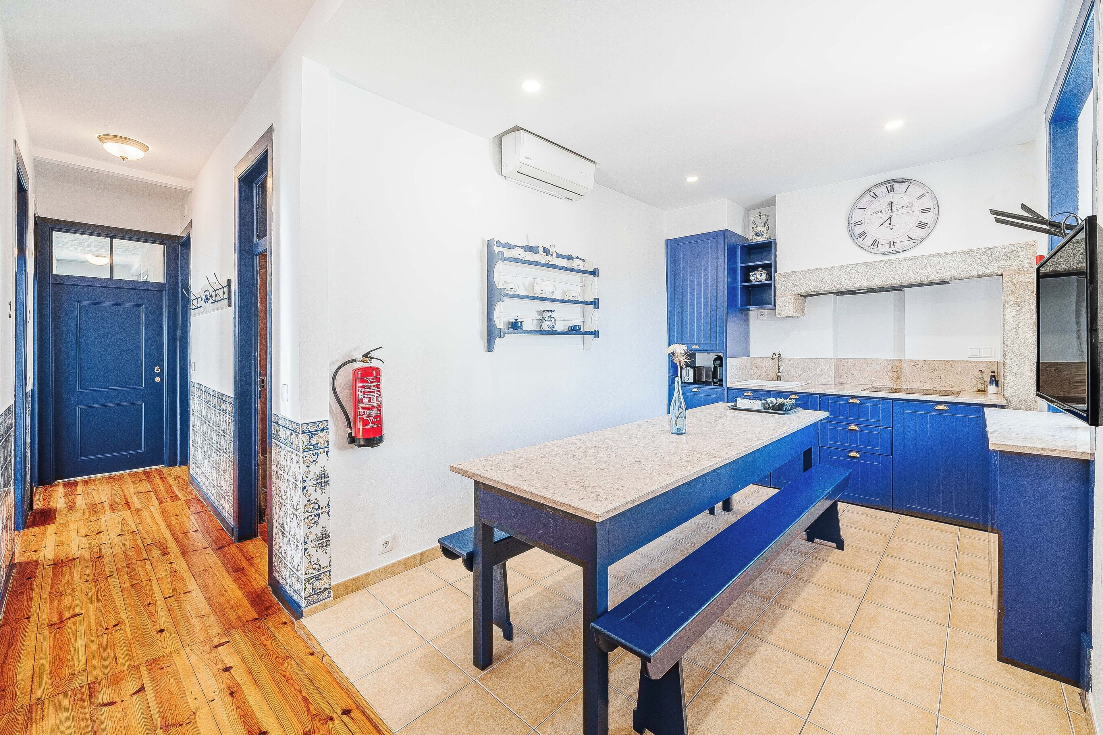 A modern kitchen with a blue and white color scheme, a wooden floor, and a bench at the center.