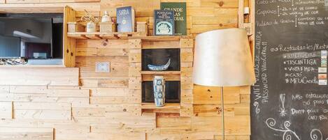 A wooden wall with shelves containing books and decorative items, a television, and a chalkboard with written information.