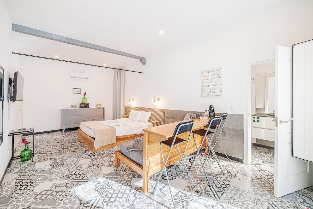Un dormitorio con cama, escritorio y silla. Hay un armario, un espejo y una puerta que da a otra habitación.