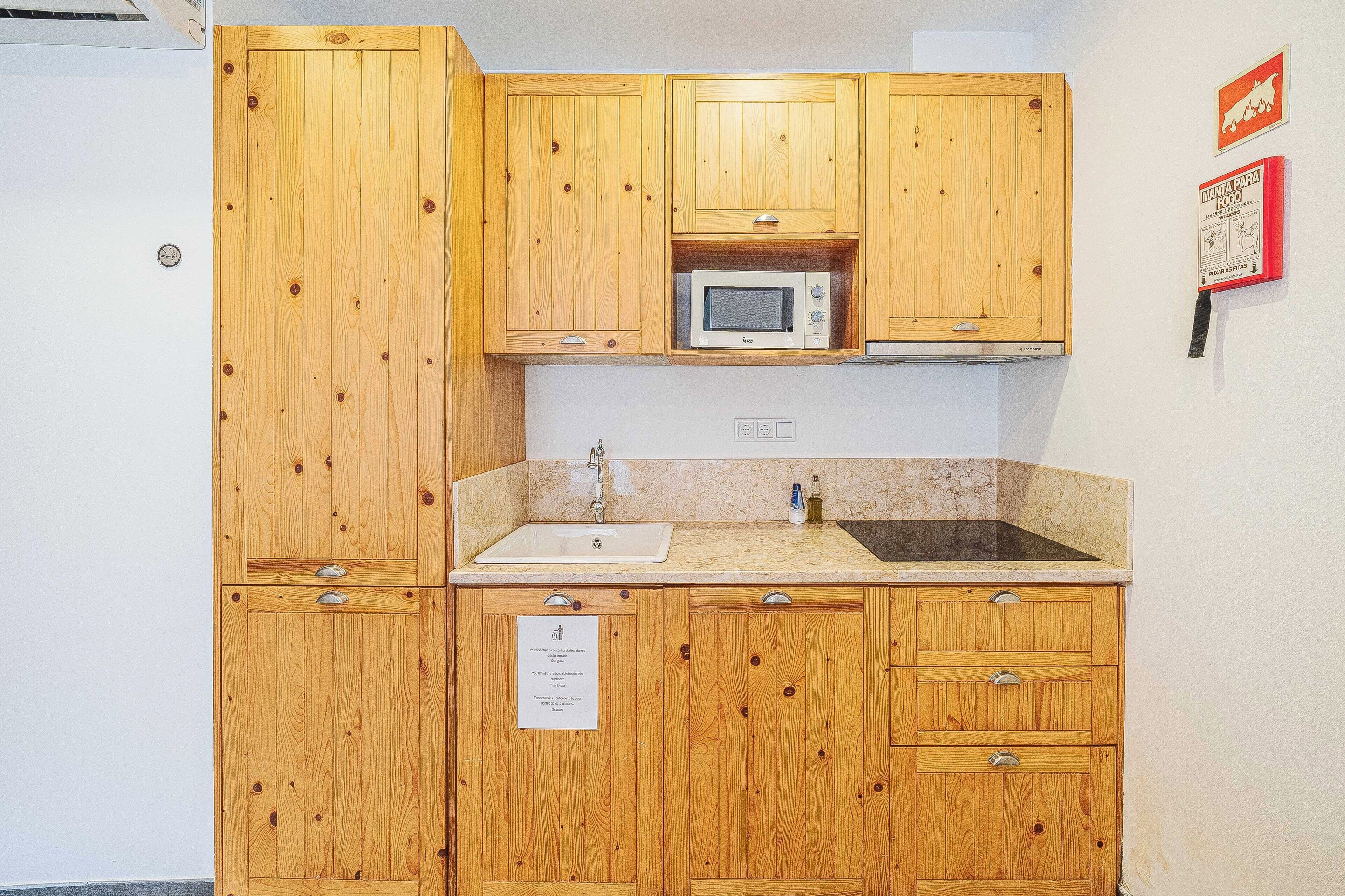 A kitchen with wooden cabinets, a microwave, a sink, and a wall-mounted sign.