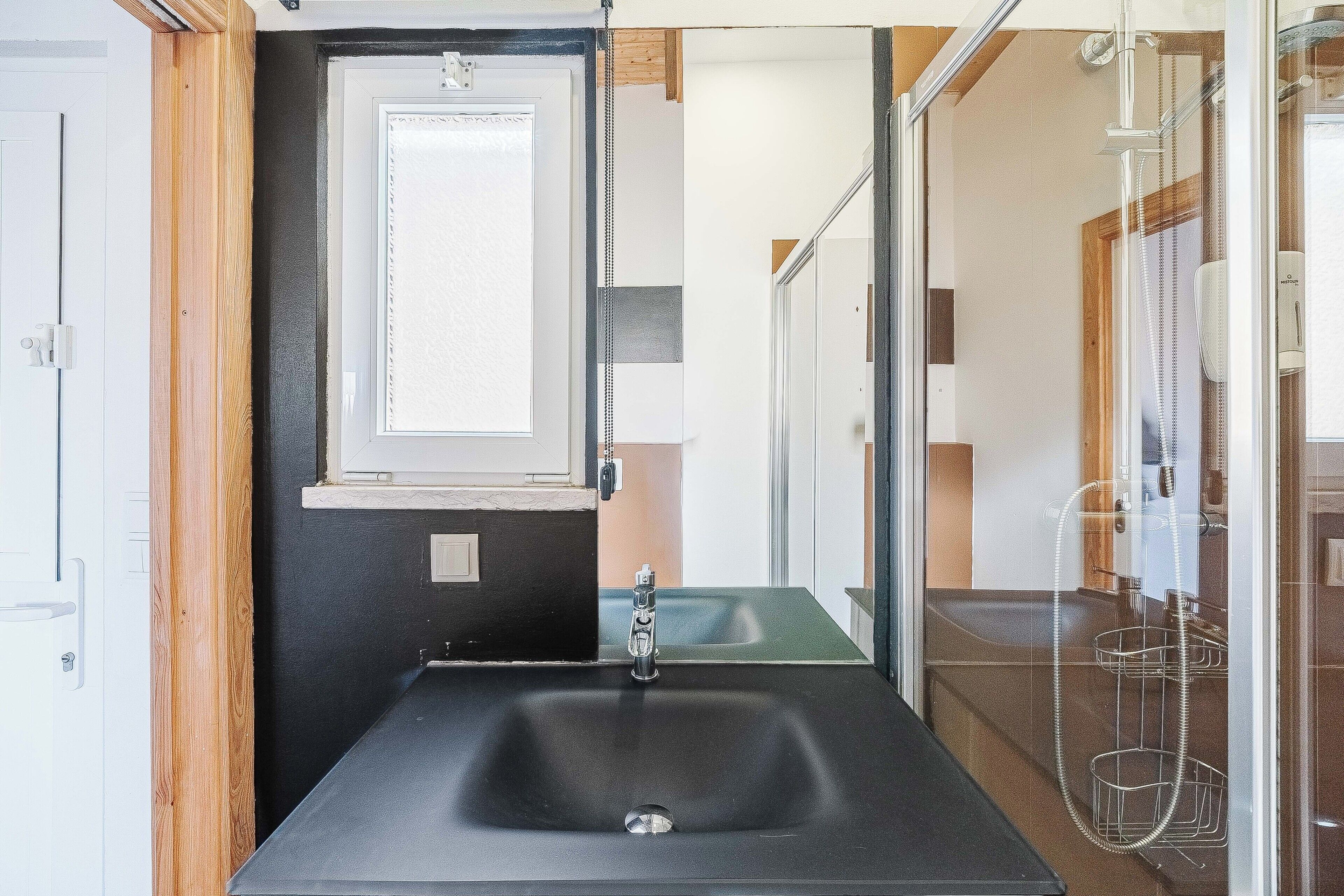 Un baño moderno con un lavamanos negro, un espejo y una zona de ducha.