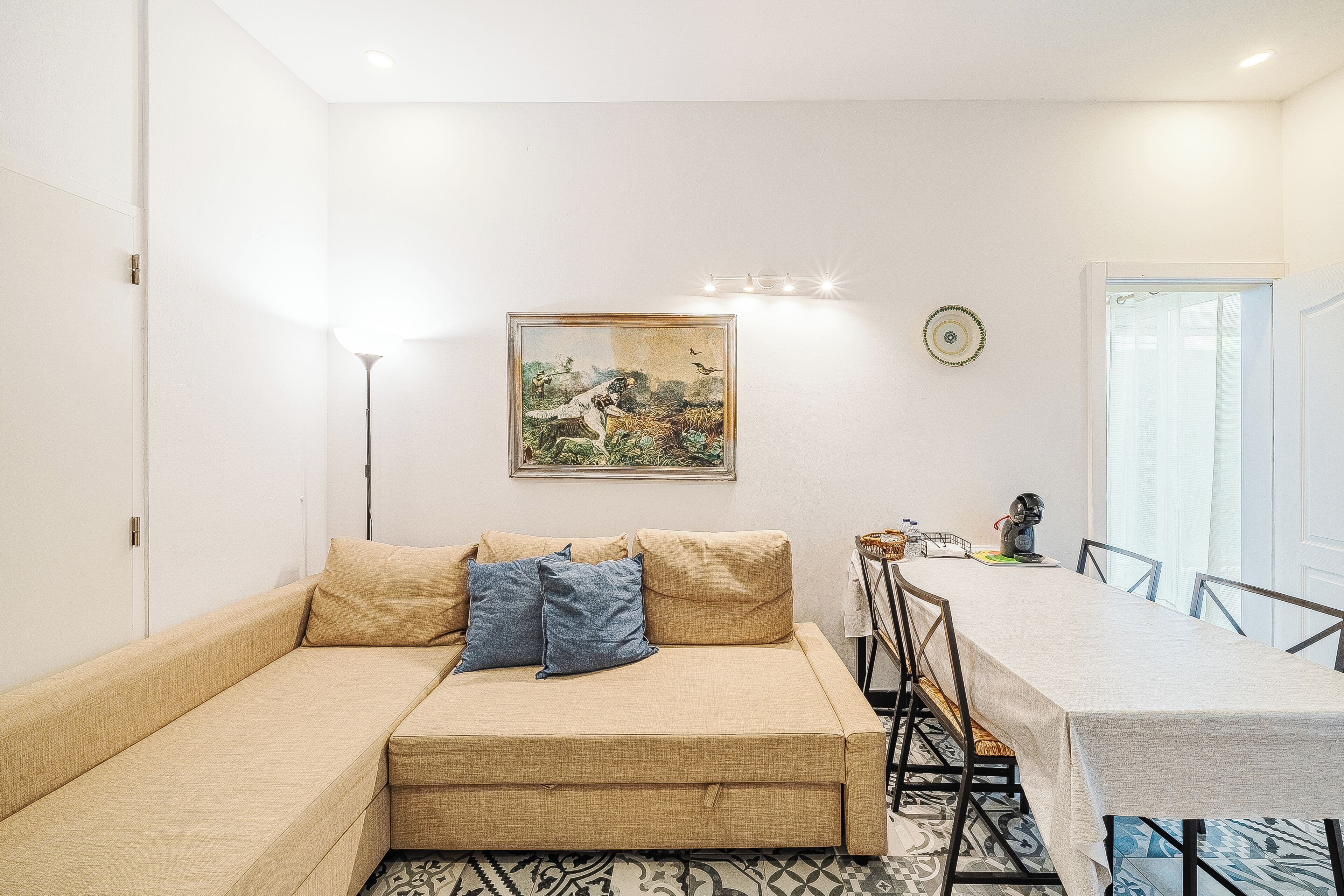 A room with a sofa, a dining table, a painting, and a lamp.