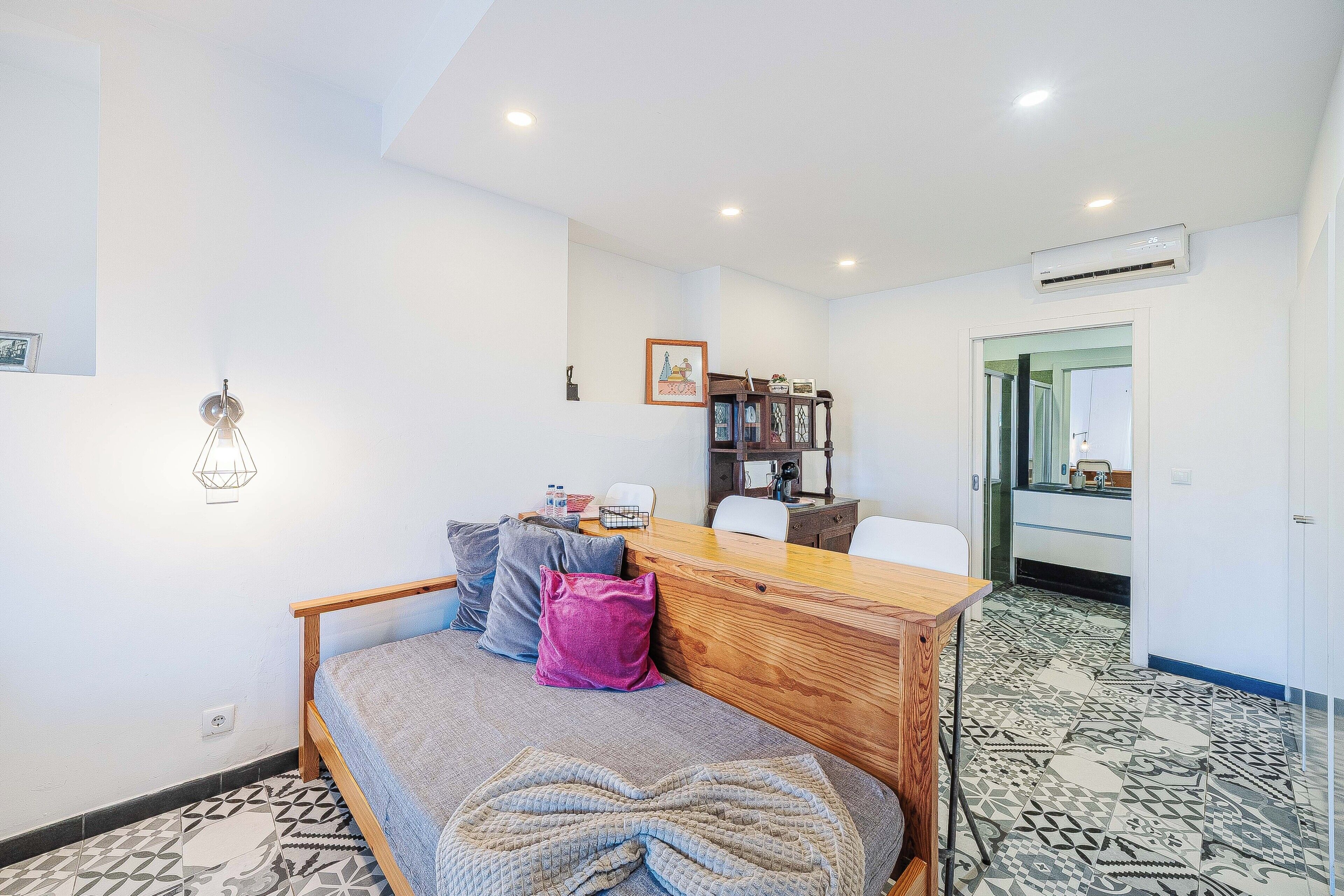 Ein Schlafzimmer mit Bett, einem Holztisch, einem Stuhl, einem Kleiderschrank und einem durch eine offene Tür einsehbaren Badezimmer.