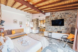 Ett hotellrum med en vägg av natursten, en platt-TV, en säng, en soffa, en matplats och ett kök.