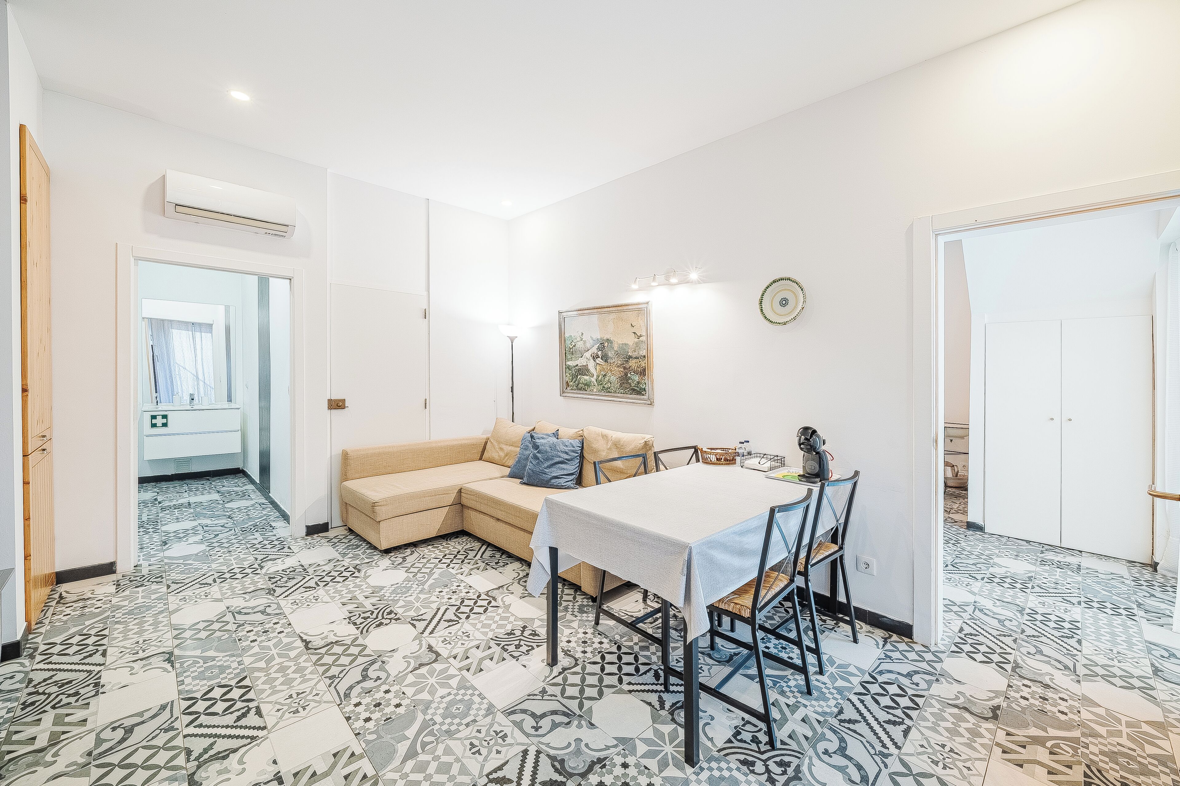 Una habitación con una mesa de comedor, un sofá, baldosas de suelo estampadas y un equipo de aire acondicionado.