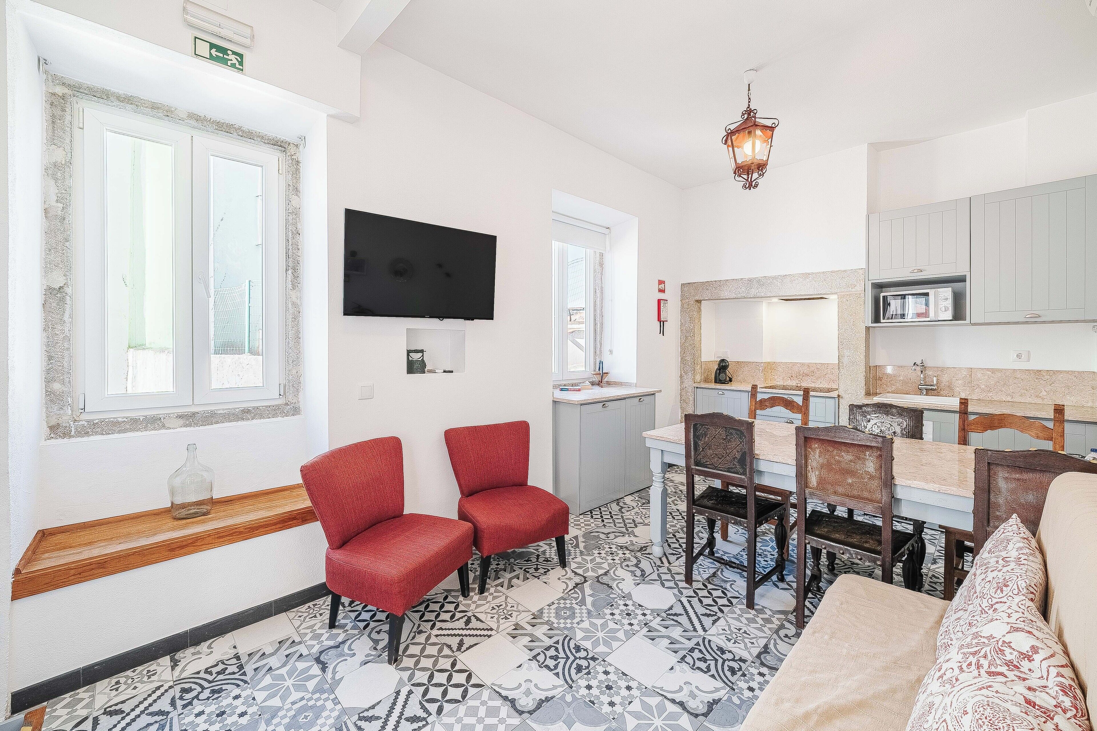 A living room with a TV, two red chairs, a sofa, a patterned floor, and a dining area with a table and chairs.