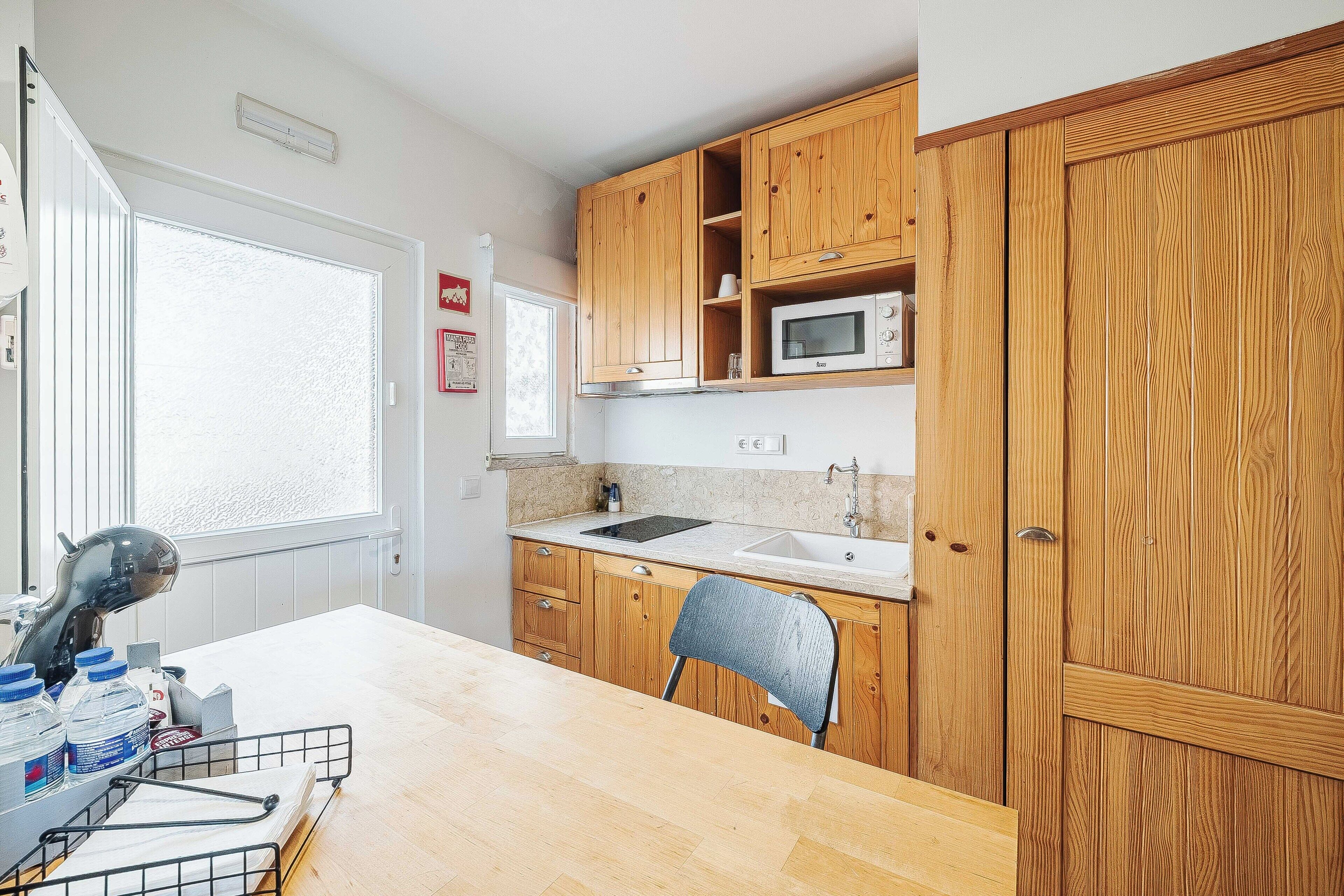 A kitchen with wooden cabinets, a microwave, a sink, and a chair.