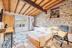 Un dormitorio con cama, una silla, una mesa, un muro de piedra y un techo de madera.