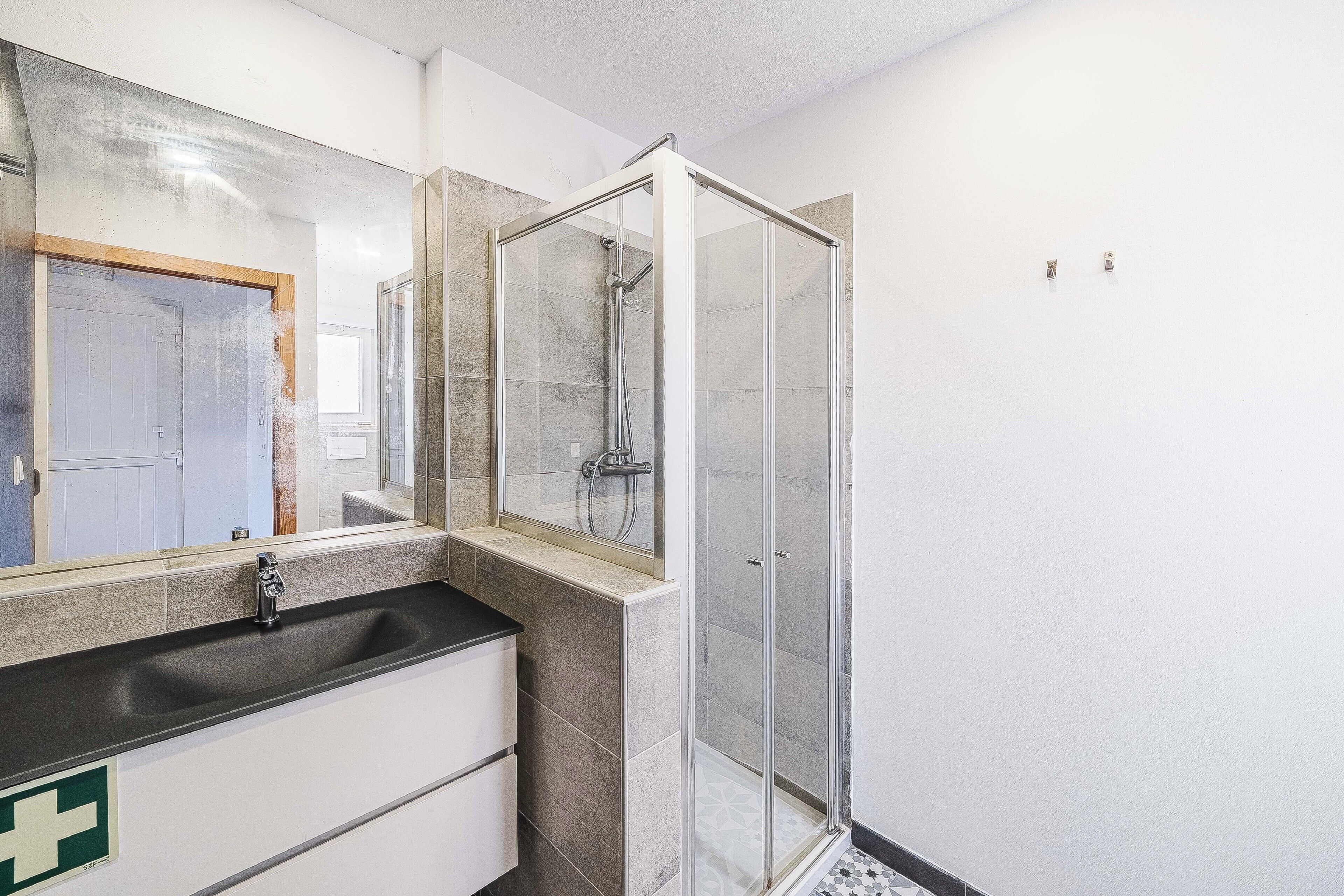 A bathroom with a glass shower enclosure, a sink with a mirror, and a cabinet below.