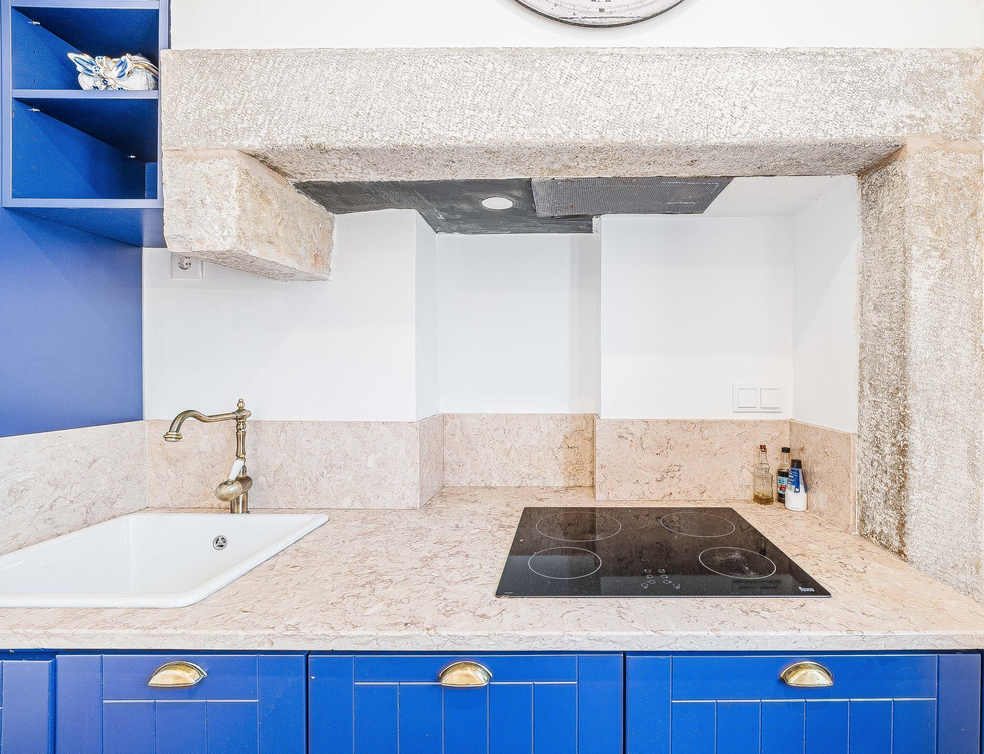A kitchen with a sink, stove, blue cabinets, and a clock on the wall.