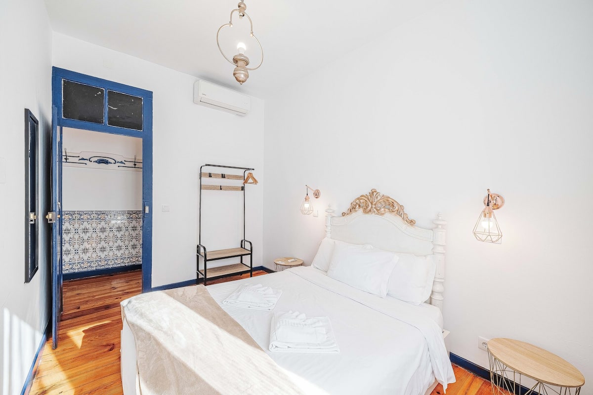 Un dormitorio con una cama, una mesita de noche, una lámpara de pared y una puerta que da a otra habitación.