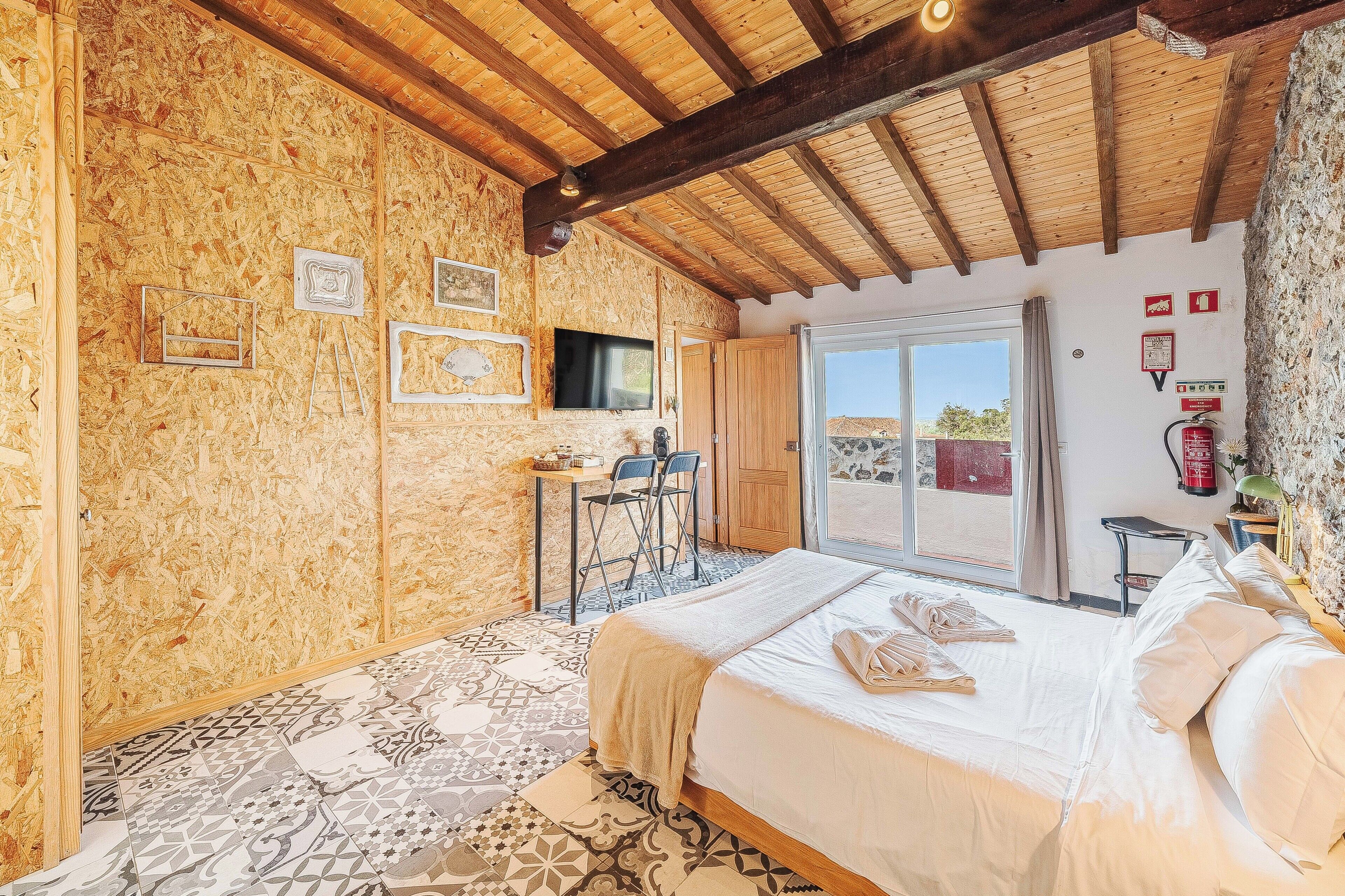 Un dormitorio con techo de madera, cama, escritorio y televisor.
