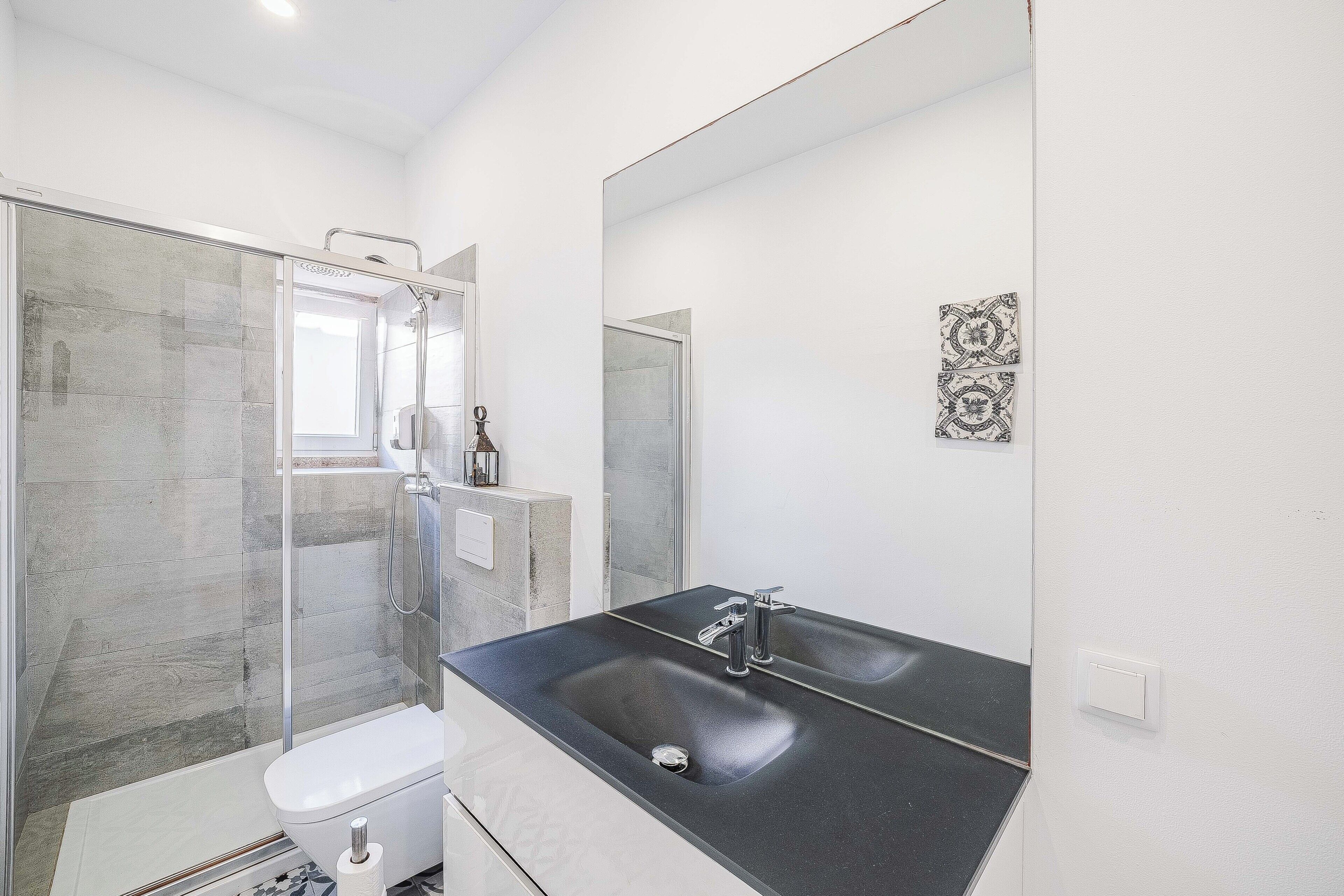 A modern bathroom with a glass-enclosed shower, a black sink, and a large mirror.