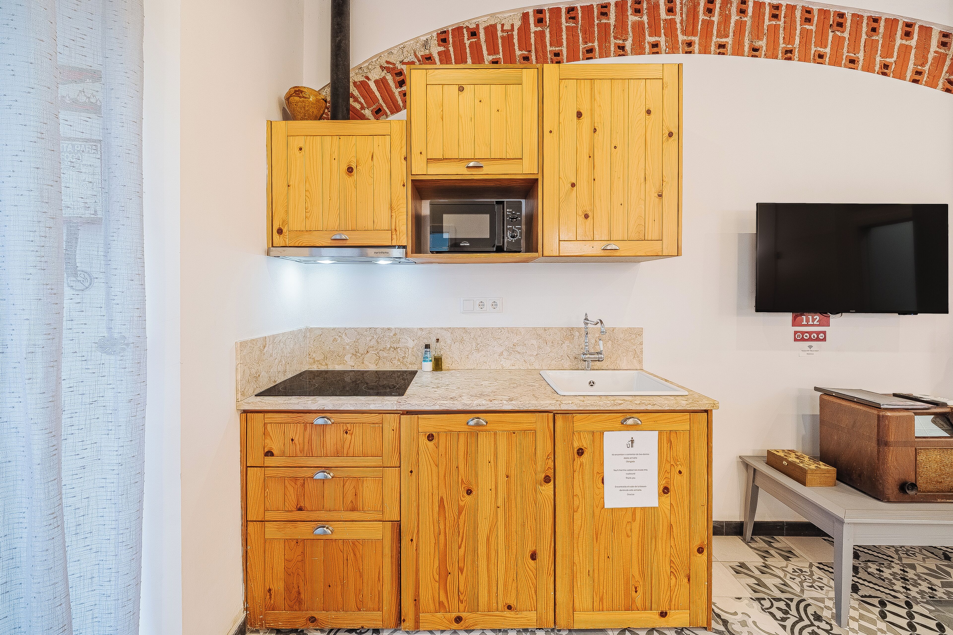 Una cocina con gabinetes de madera, microondas, pileta y televisor.