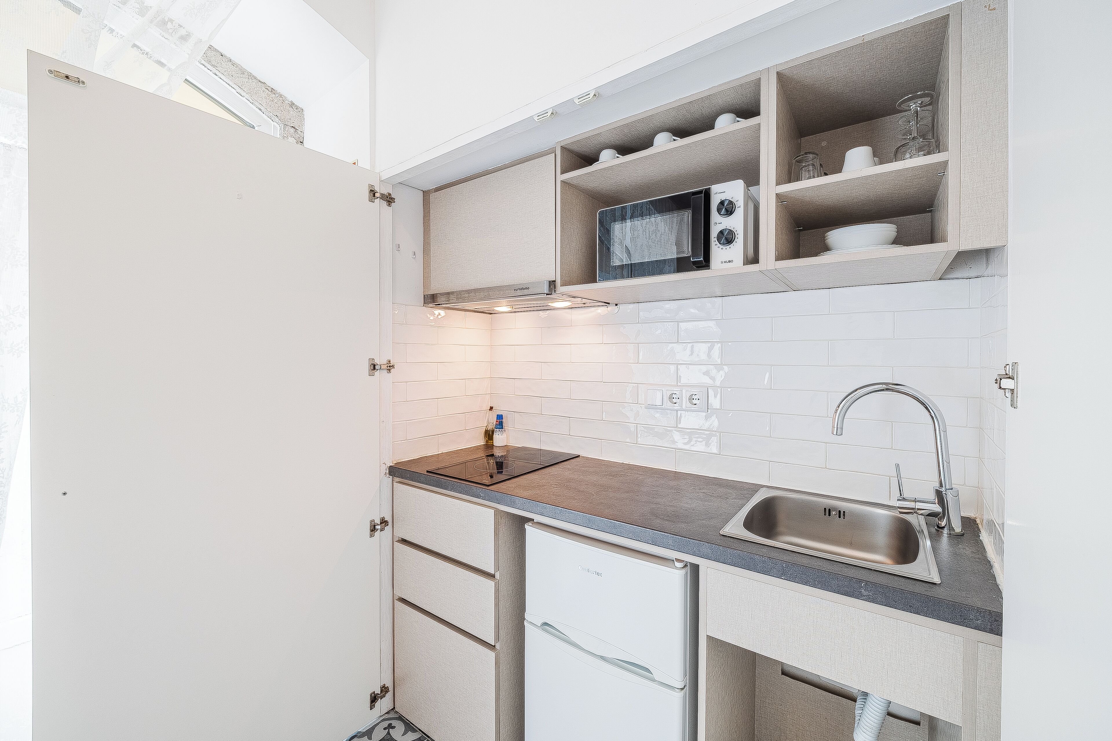 A compact kitchen with a built-in microwave, a sink, and a small refrigerator.